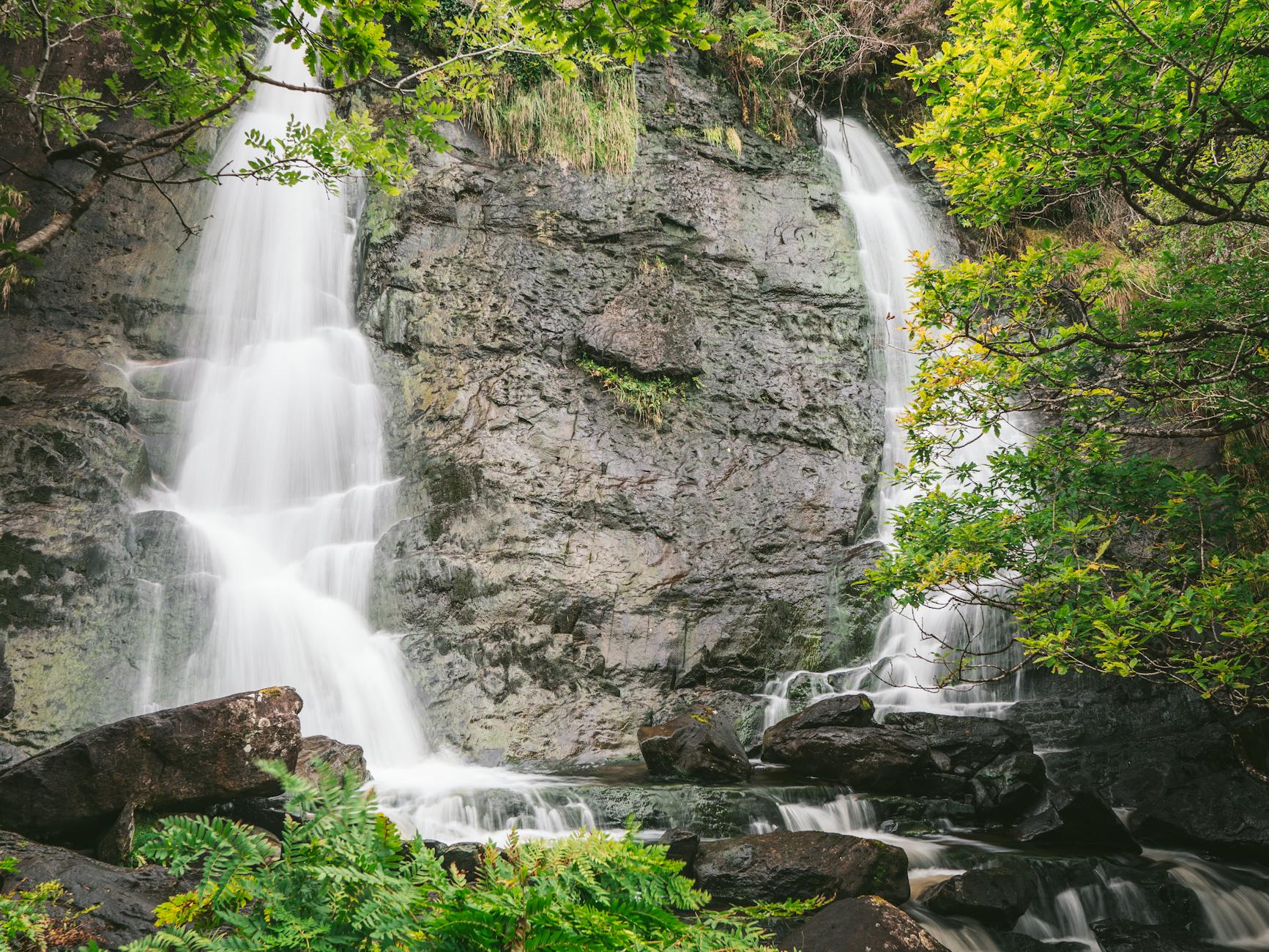 Beautiful cascading waterfall amidst lush greenery at Killarney National Park, Ireland.