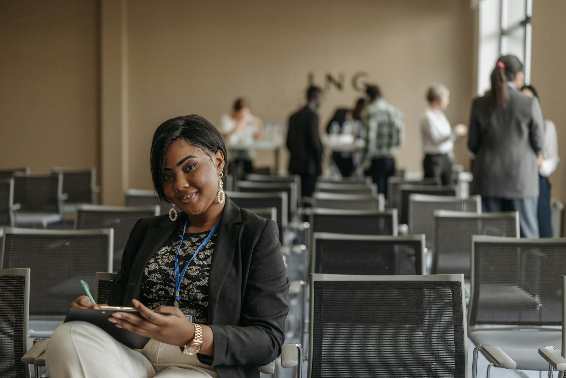 Businesswoman smiling while taking notes at a conference room event. Bright and professional setting indoors.