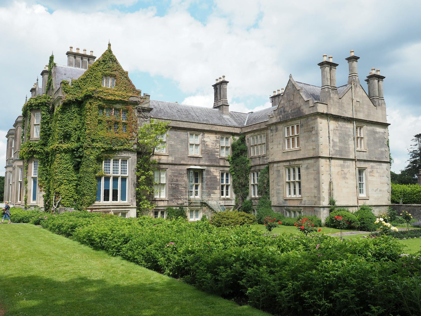 Beautiful stone mansion with ivy-covered walls and lush garden, exuding historic charm.