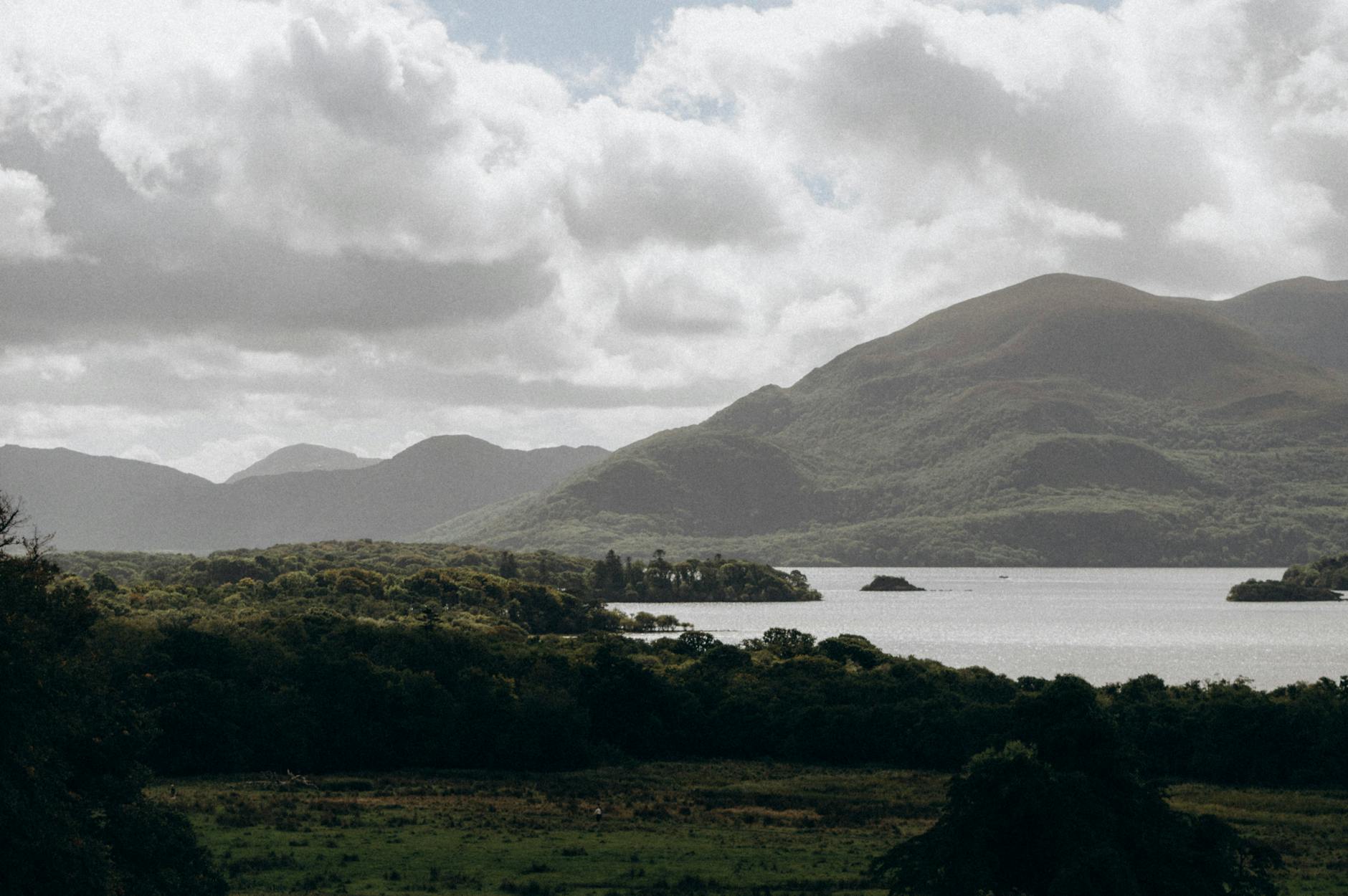 Tranquil landscape of a lake amidst lush green mountains and cloudy sky.