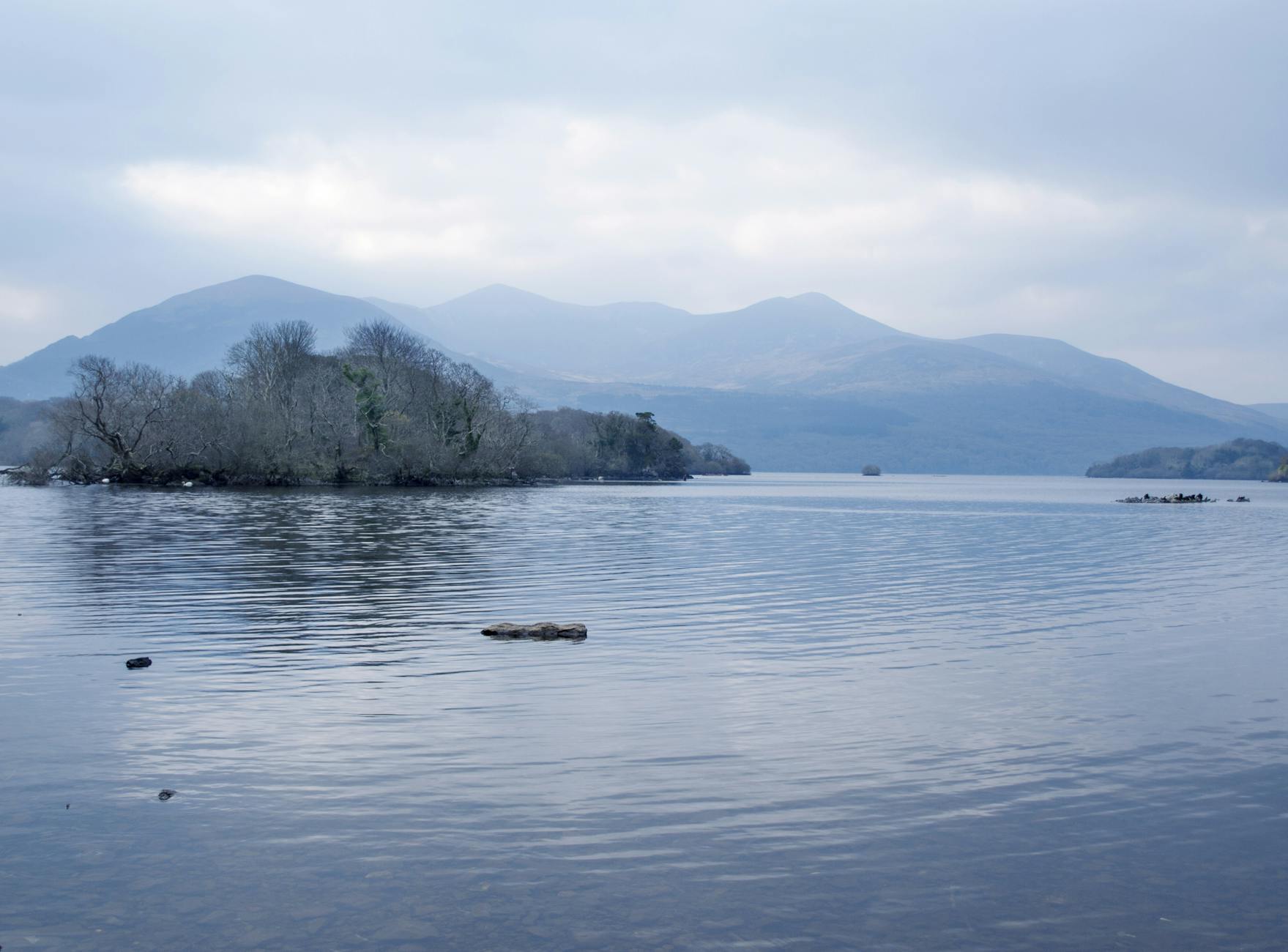 Tranquil lake and mountain scene in Killarney National Park, Ireland under a cloudy sky.