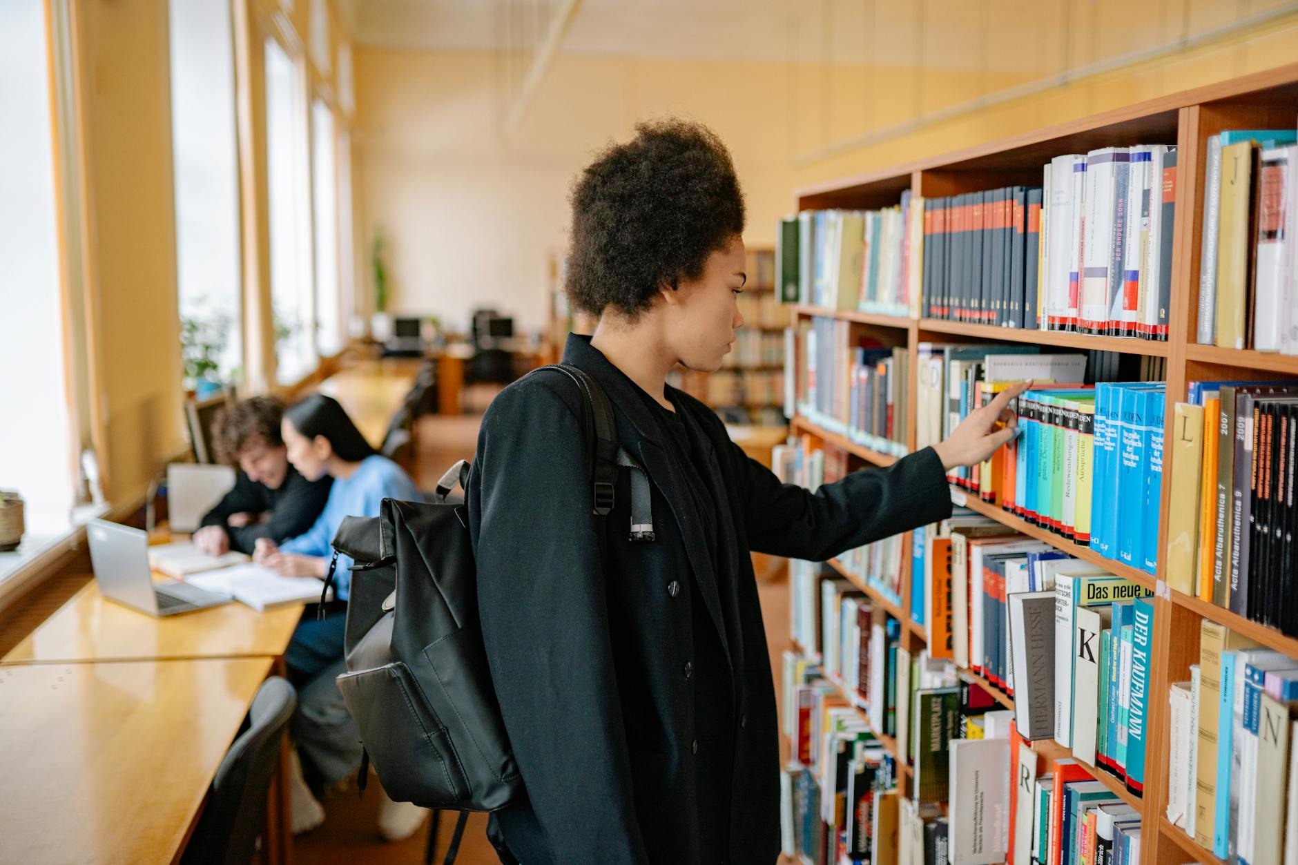 Student with backpack selecting a book in a university library