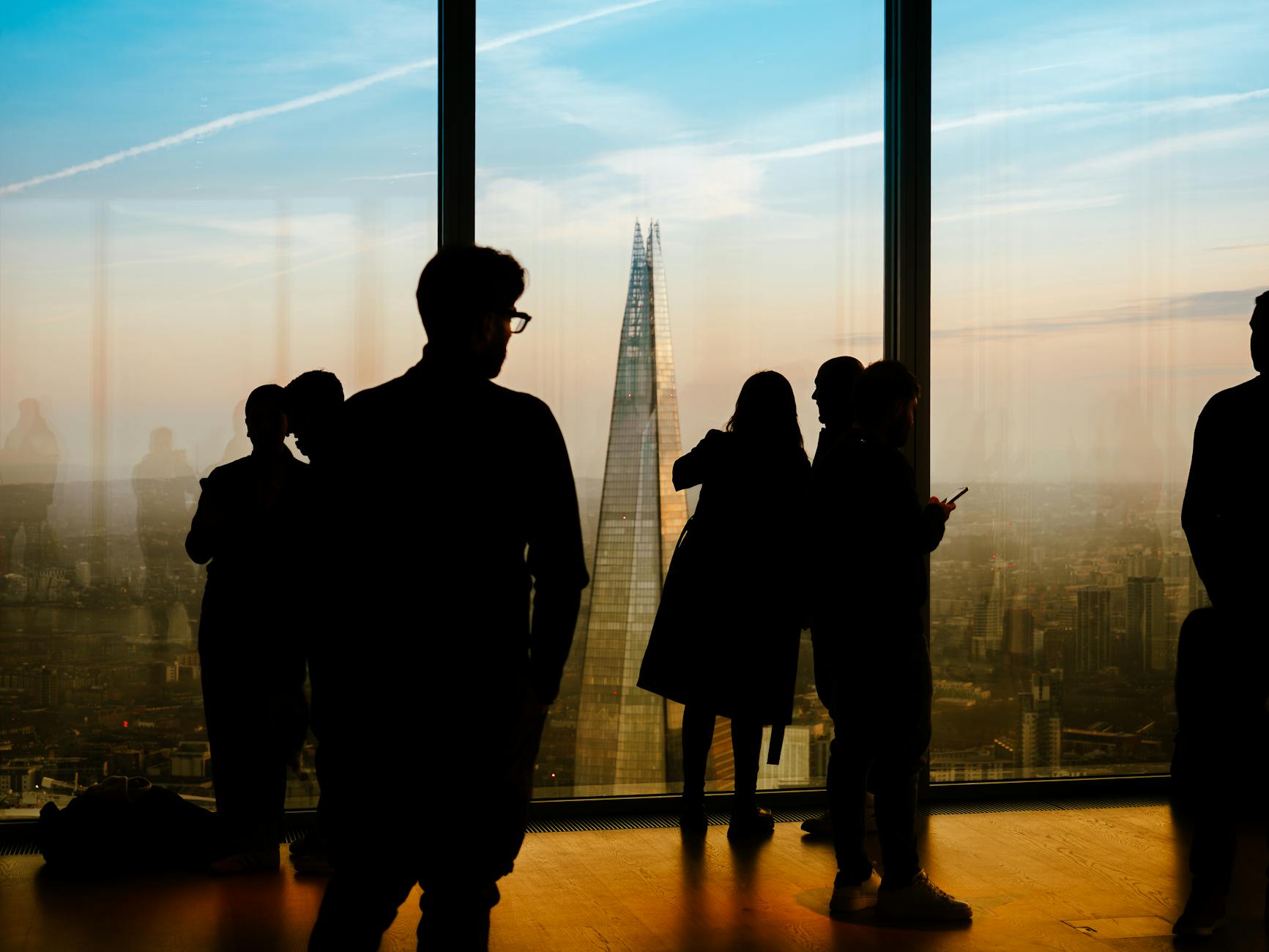 People silhouetted by a London skyline window at sunset
