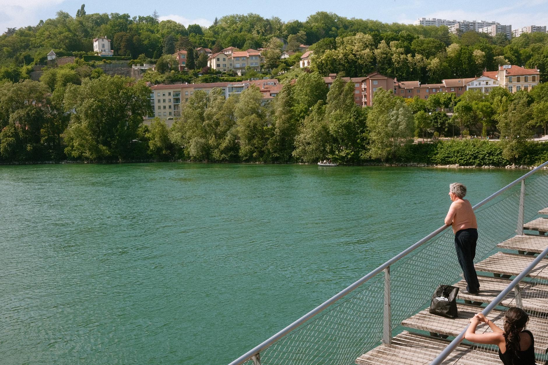 Traveler looking across the Rhone River in Lyon from a green riverbank