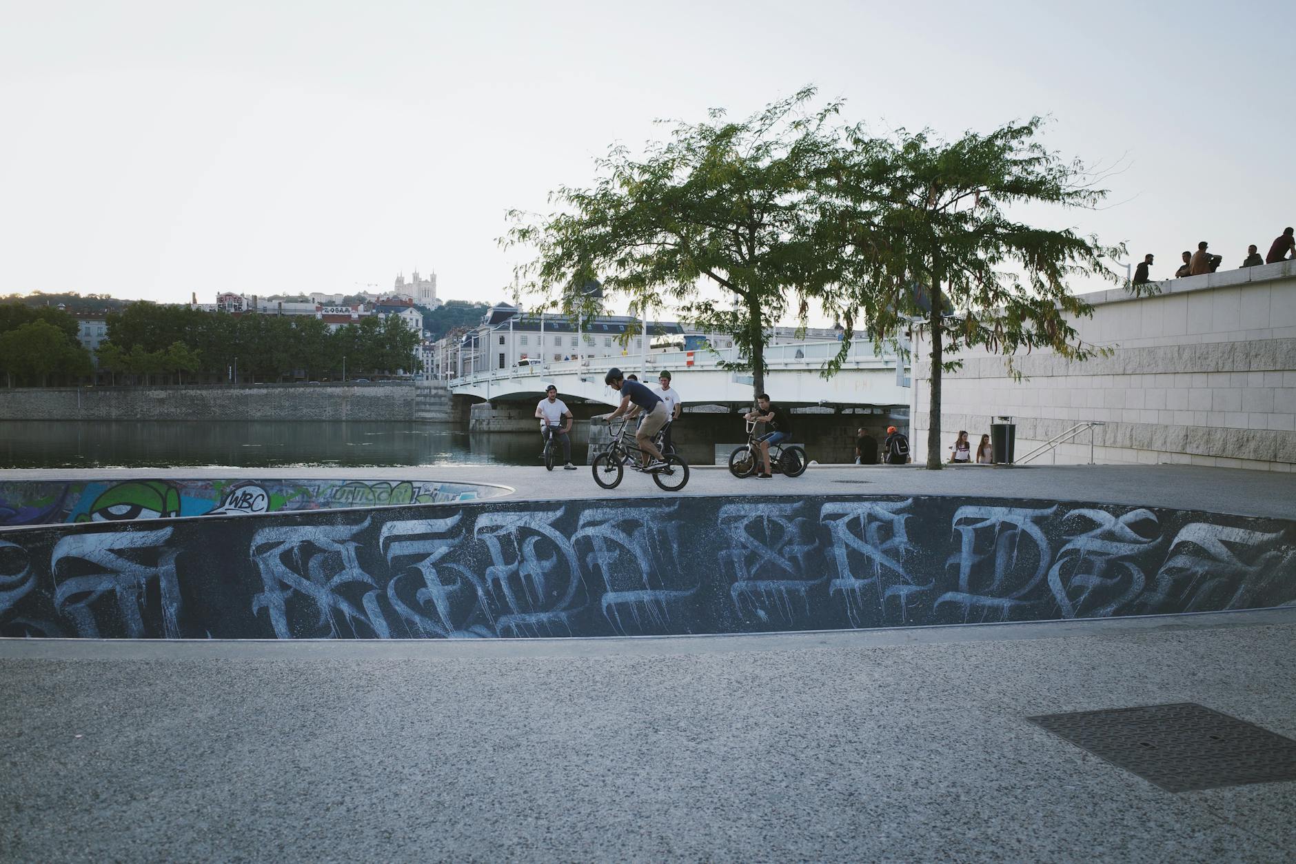 BMX riders at a riverfront skatepark with the city skyline behind them