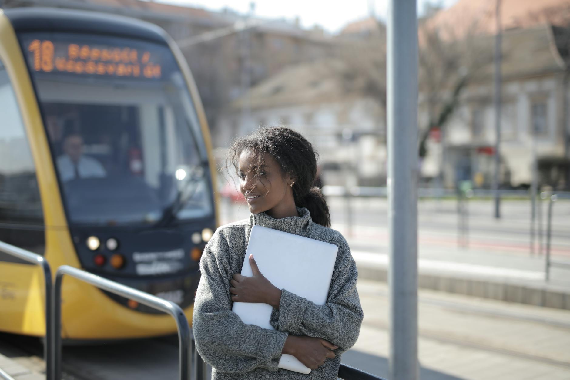 Student holding a laptop at a tram stop