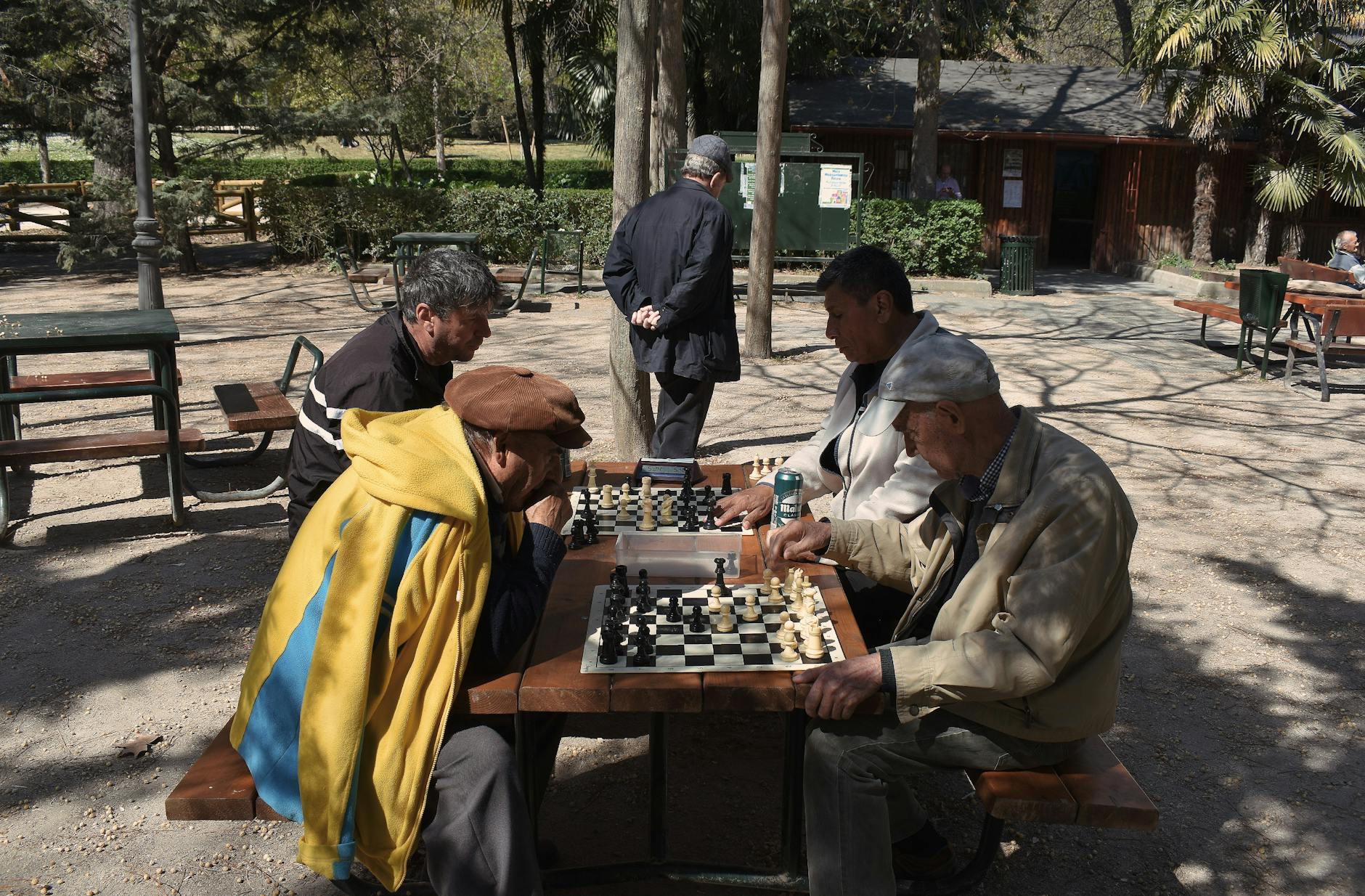 Senior men playing chess outdoors in a sunny Madrid park