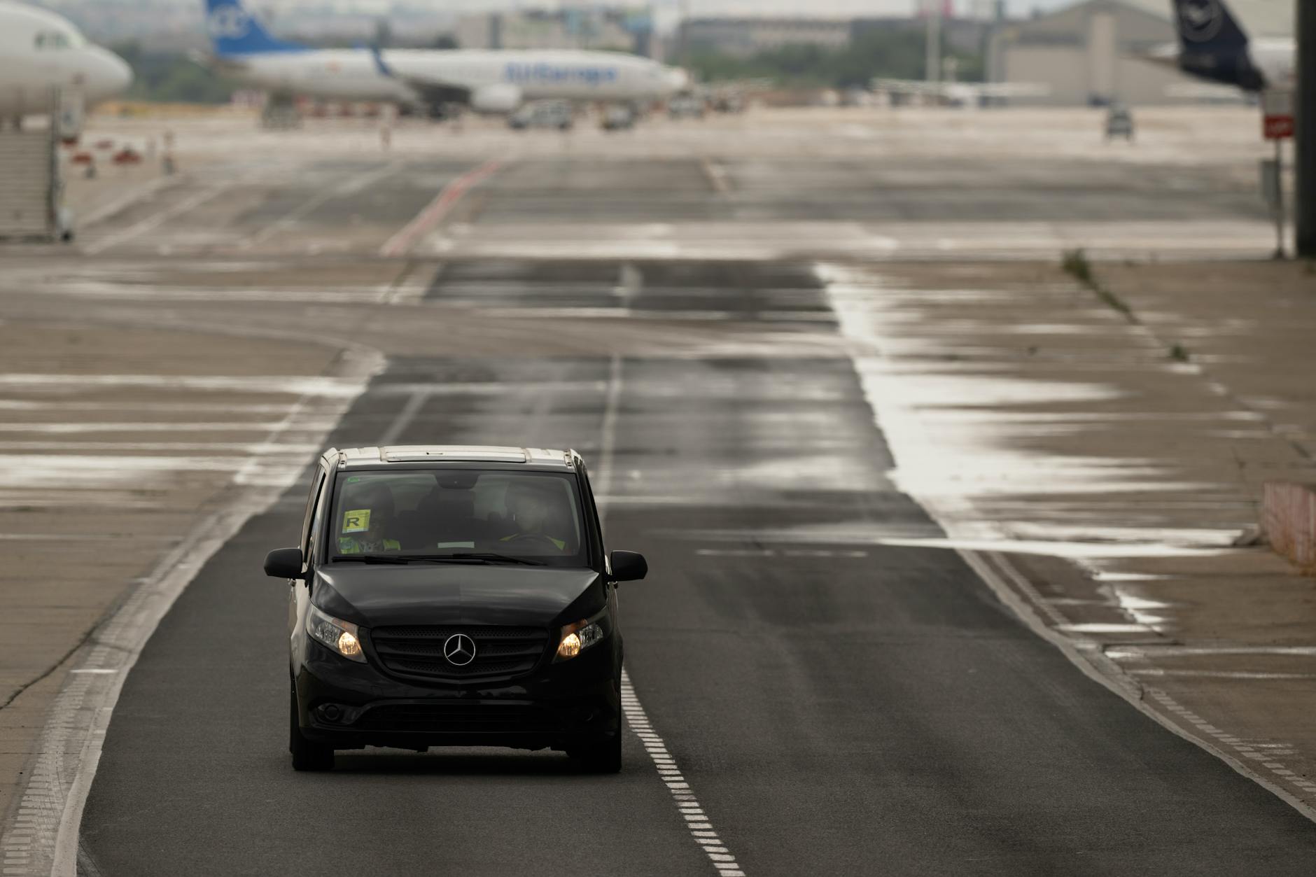 Vehicle on a rainy runway at Madrid Airport with aircraft in the background