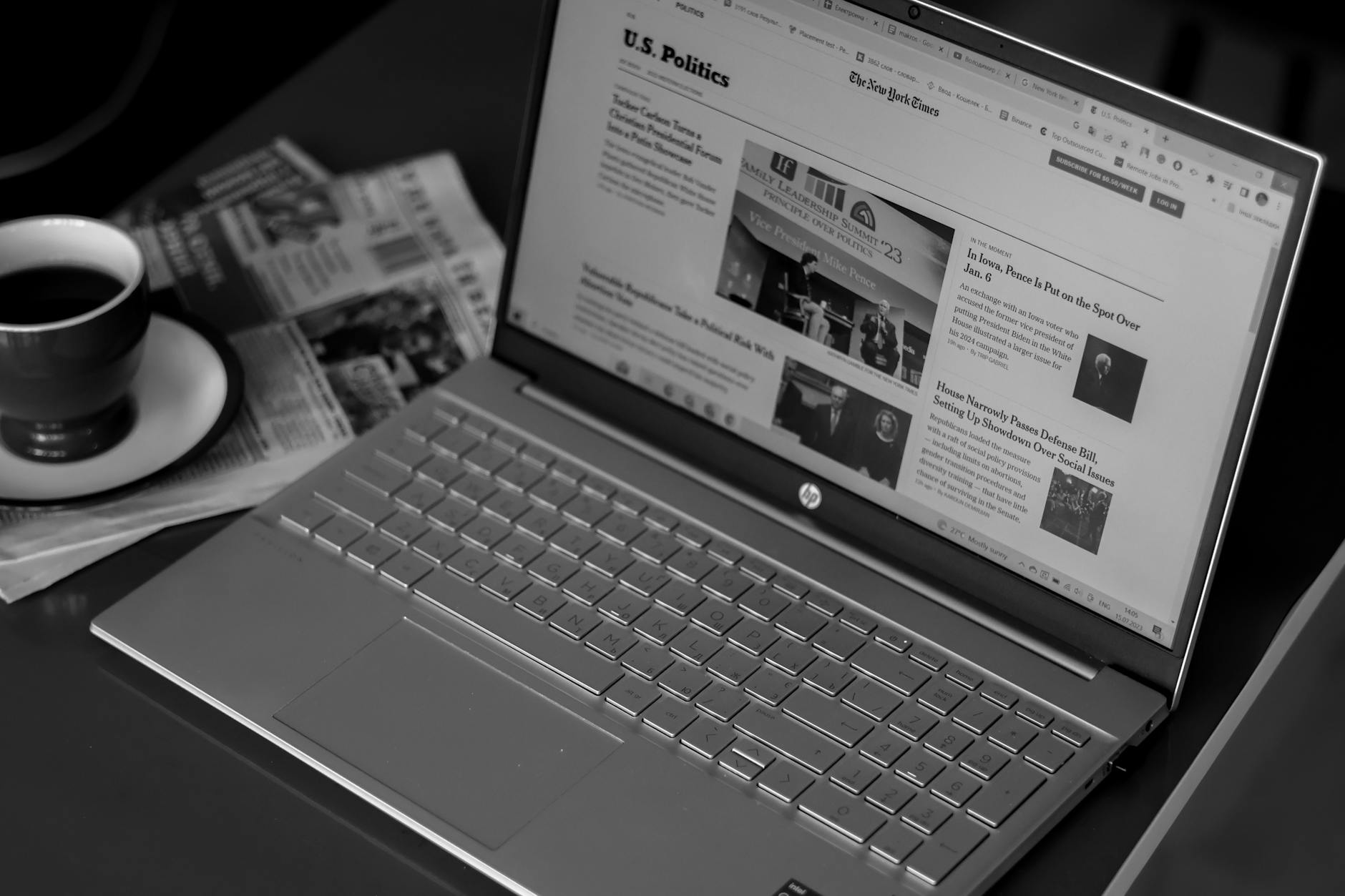 Laptop displaying news articles beside coffee and newspapers