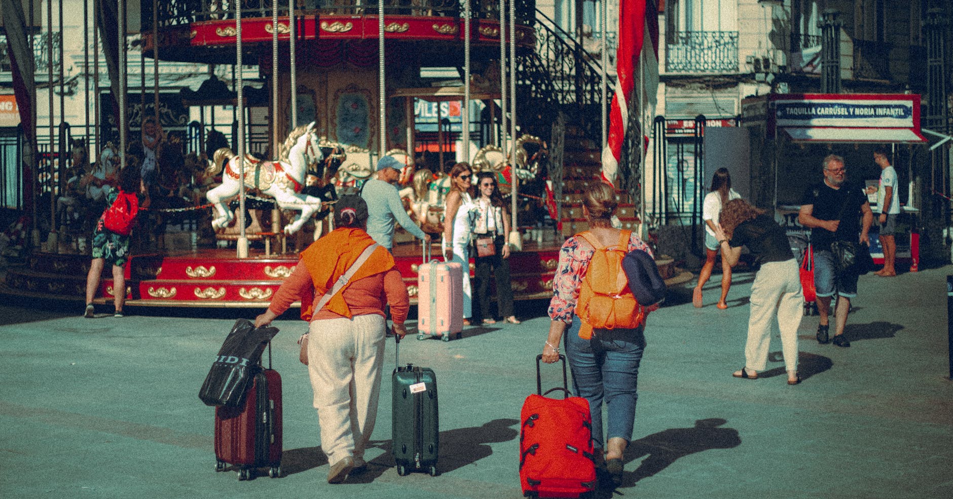 Travelers with suitcases near a city park carousel
