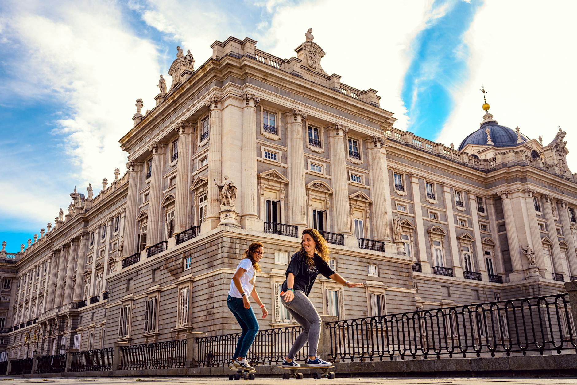 Two women skateboarding near a historic building in Madrid