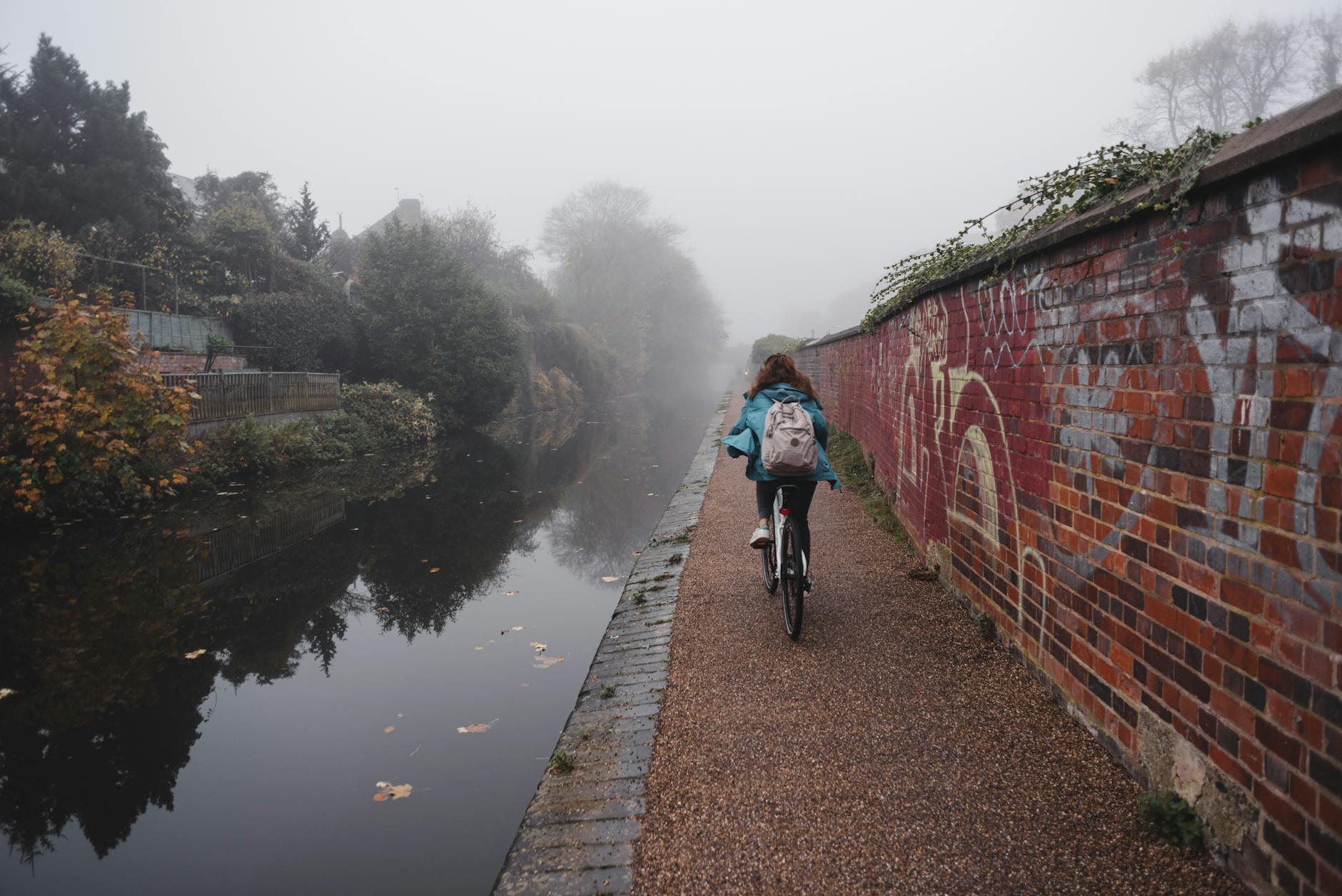Cyclist riding beside a foggy waterside canal