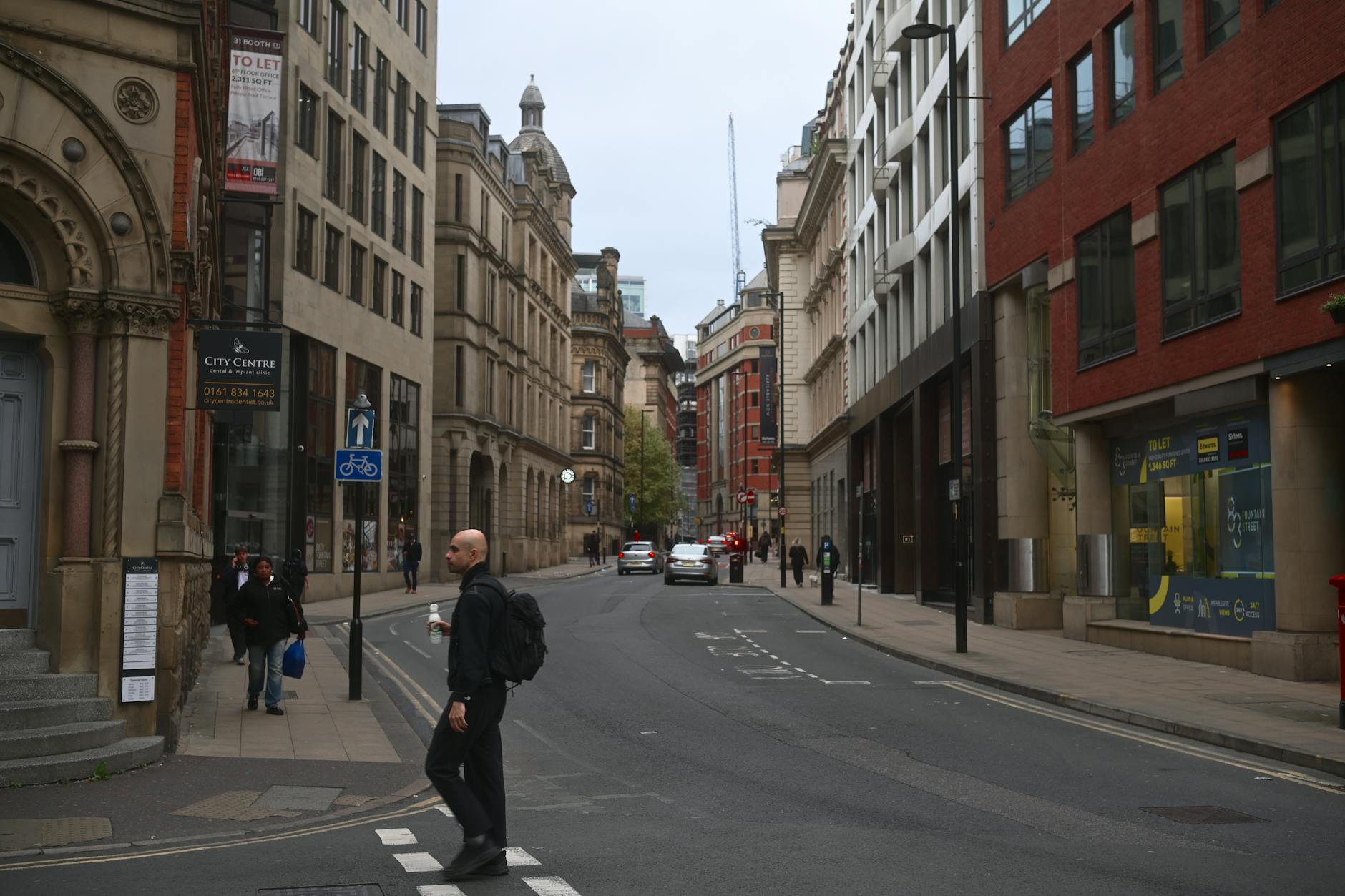 Pedestrian crossing a Manchester city-centre street near historic business architecture