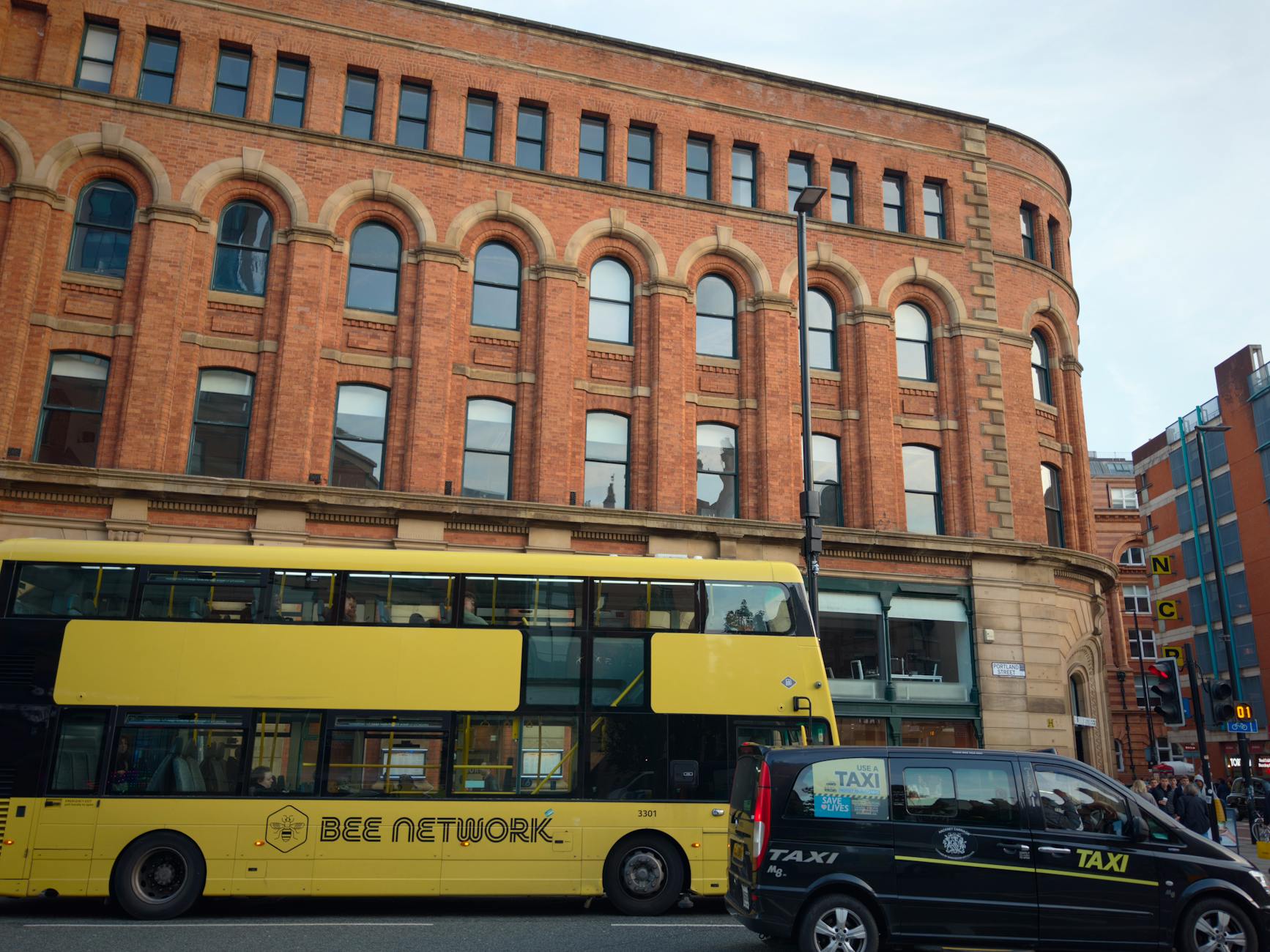 Manchester street scene with a yellow bus and taxi near historic buildings