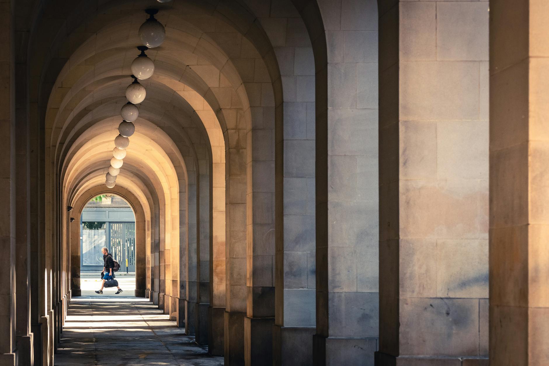 Person walking through a sunlit stone arch corridor in Manchester