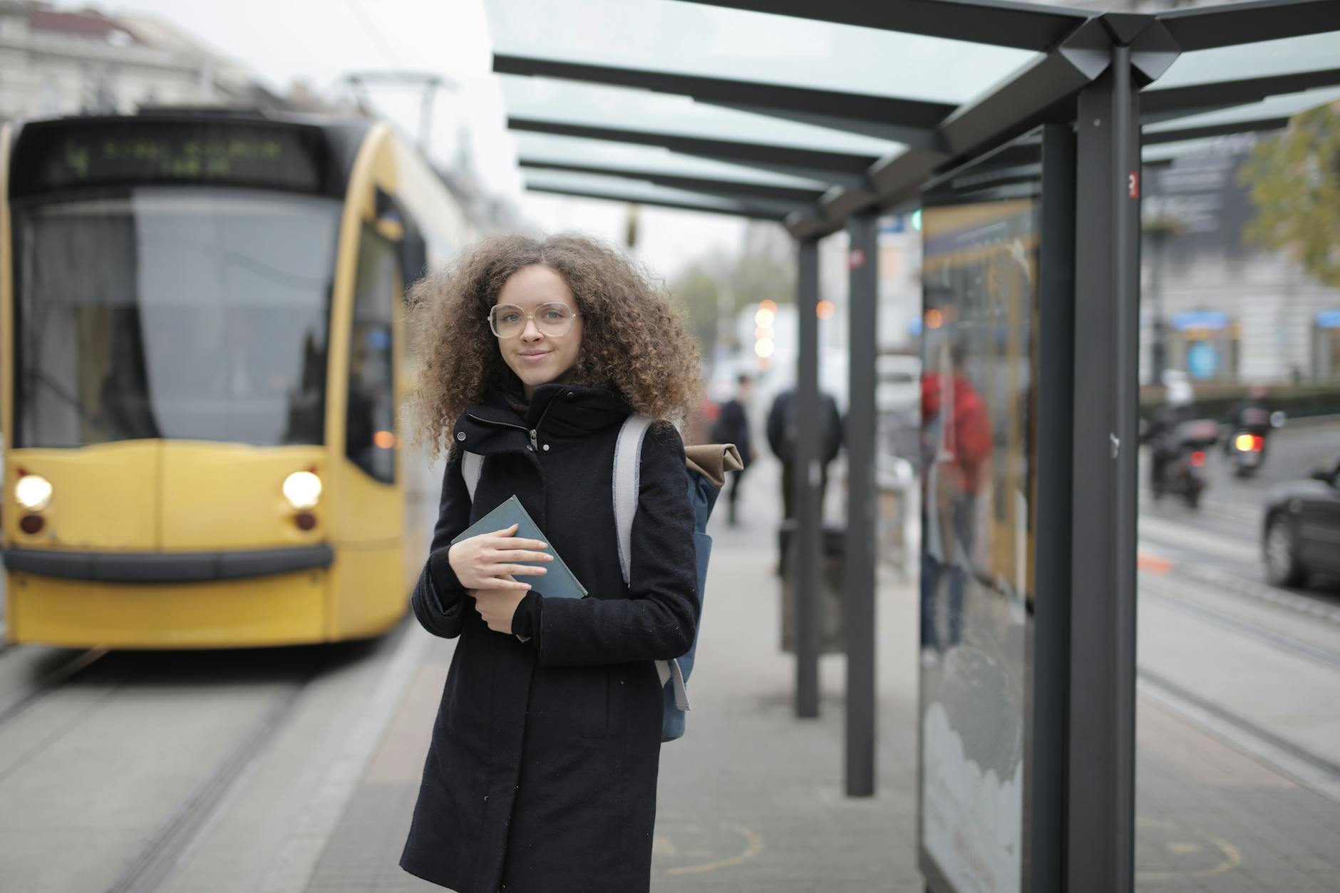Student holding a book while waiting at a tram stop