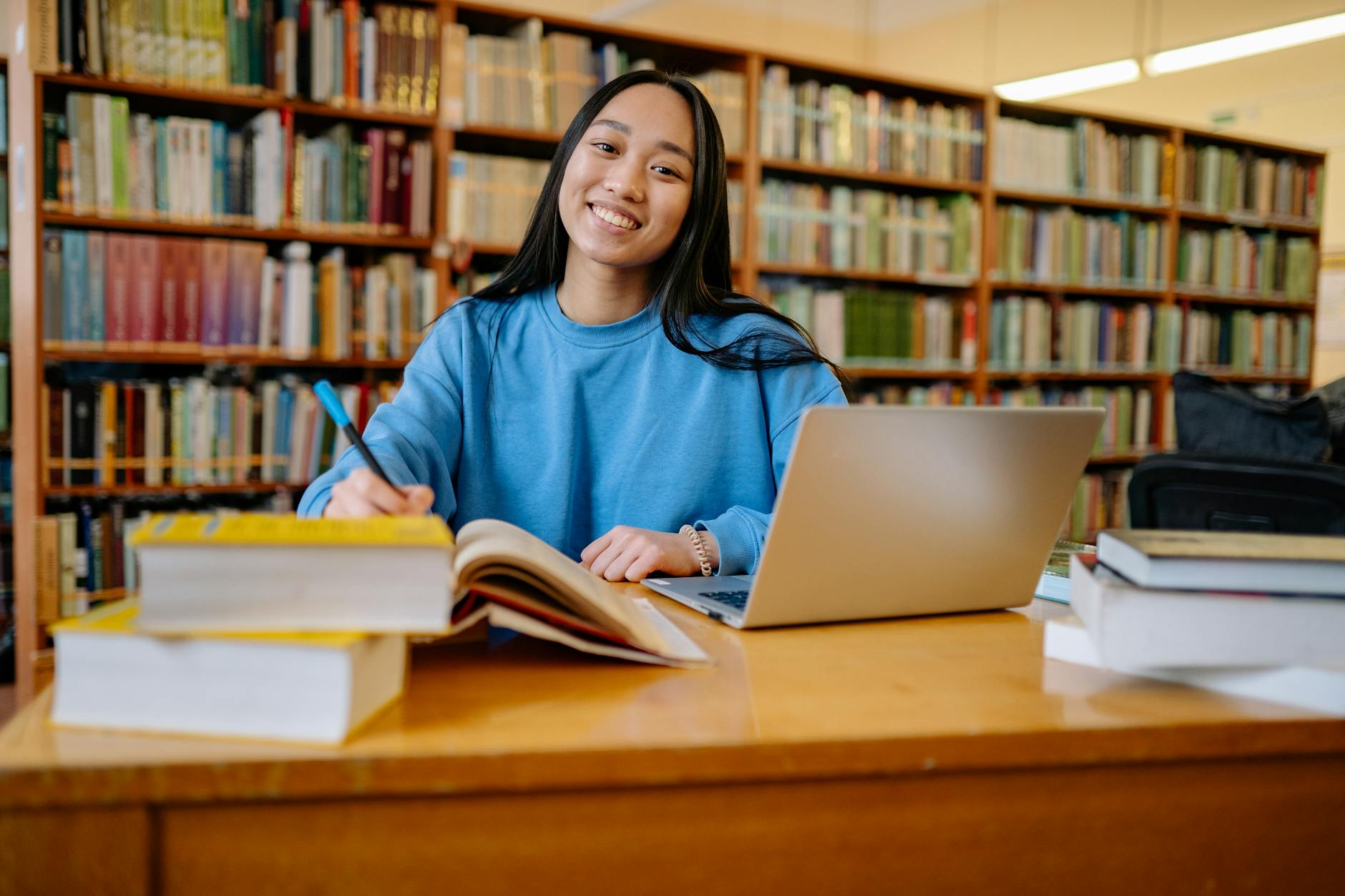 Student studying in a library with books and a laptop