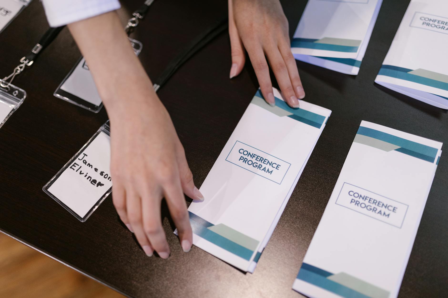 Hands organizing conference programs and name tags at a registration desk