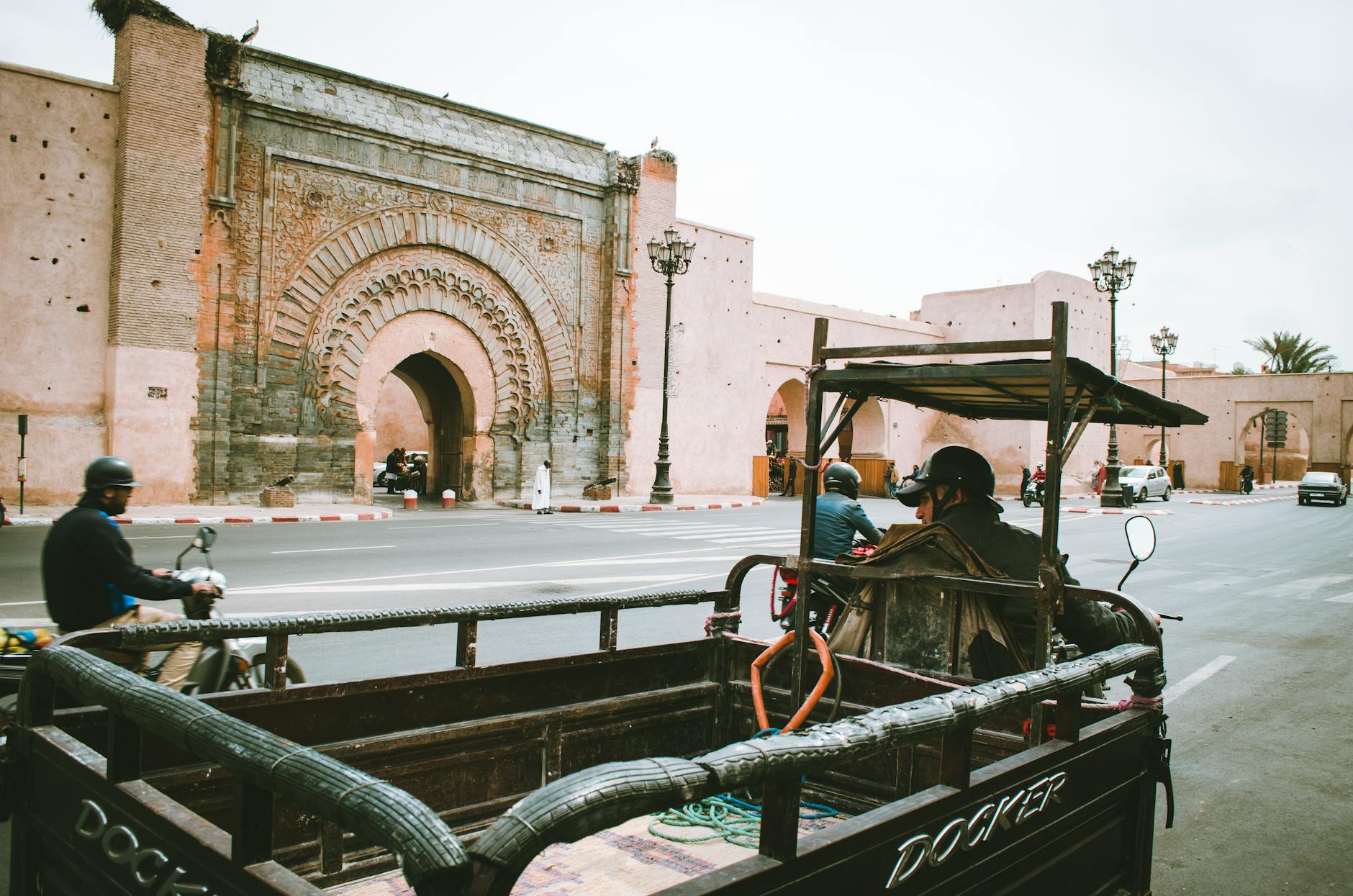 Busy Marrakech street with motorbikes and cars near an ornate gate