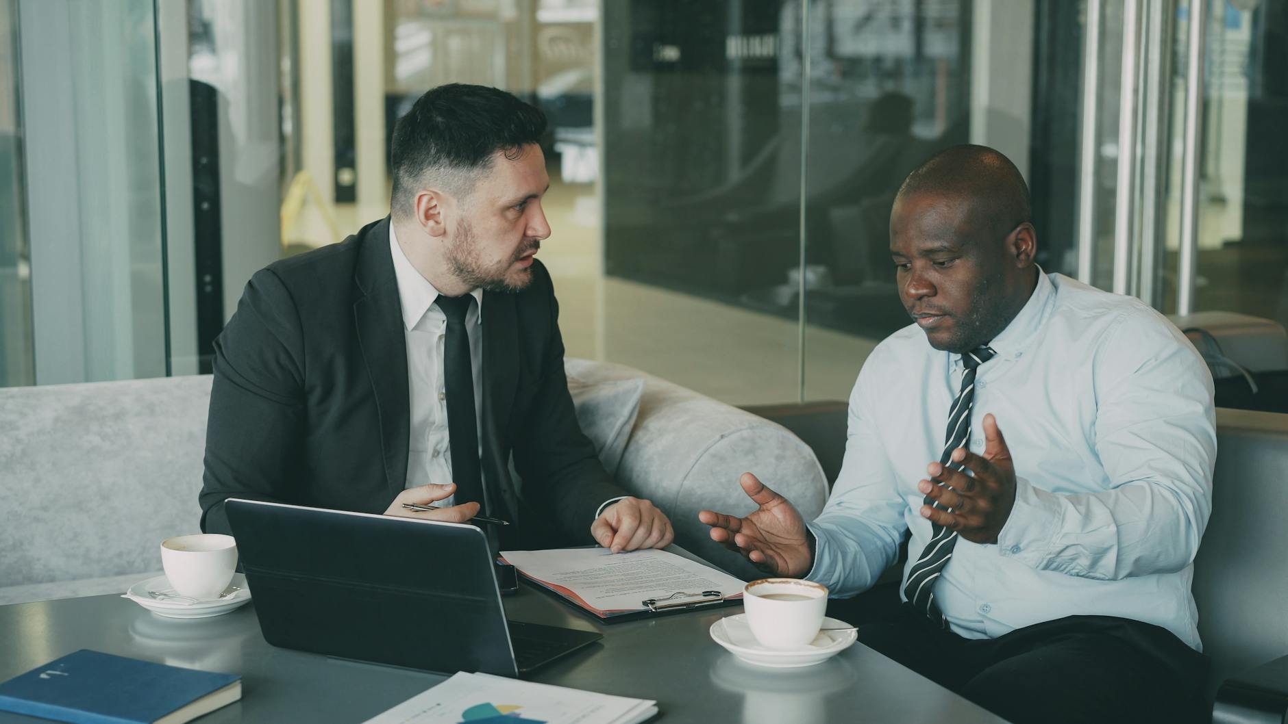 Two business colleagues discussing work over coffee and a laptop
