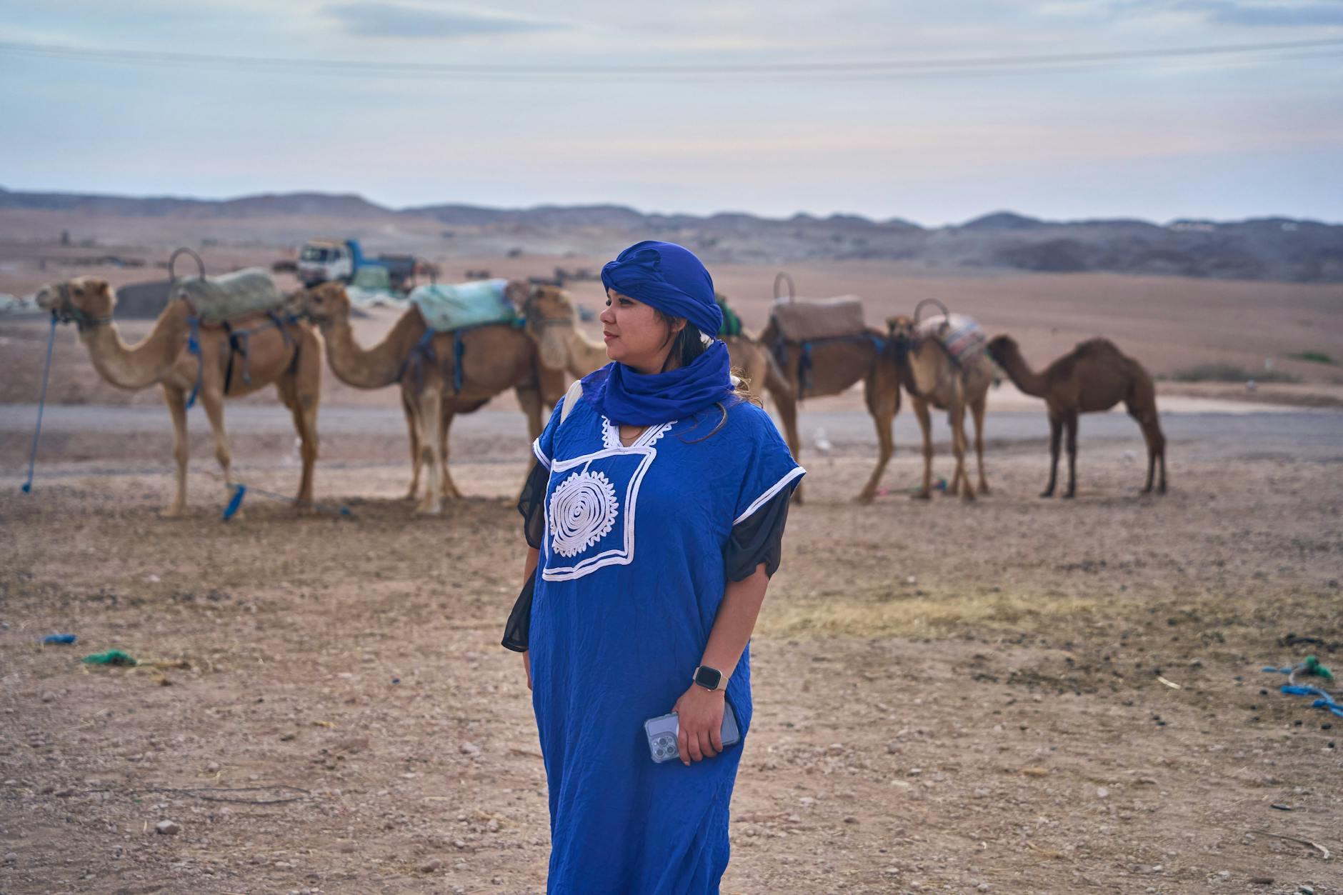 Woman in a blue robe with camels in a Moroccan desert landscape