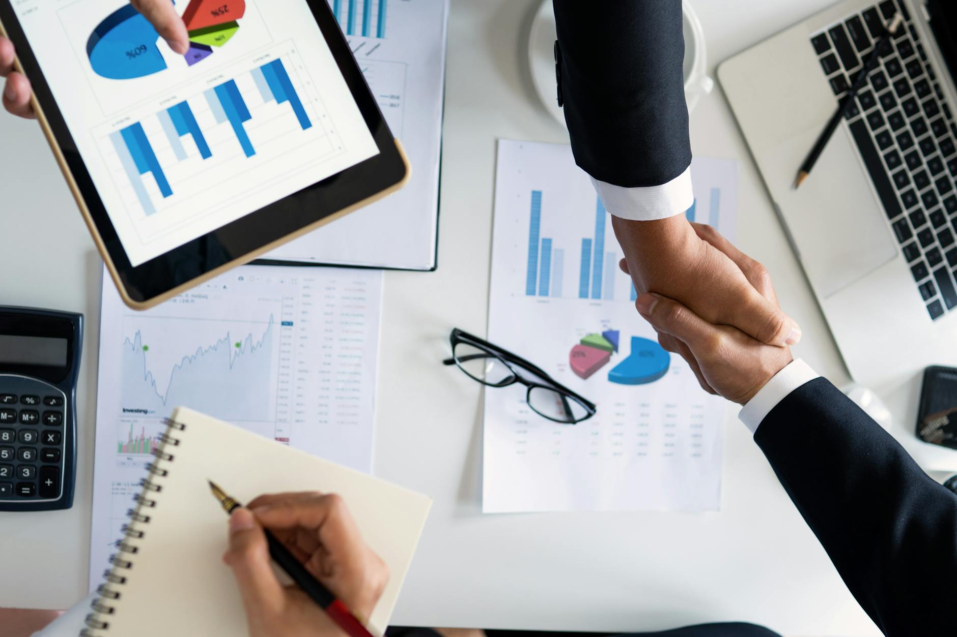 Business professionals shaking hands over graphs and charts