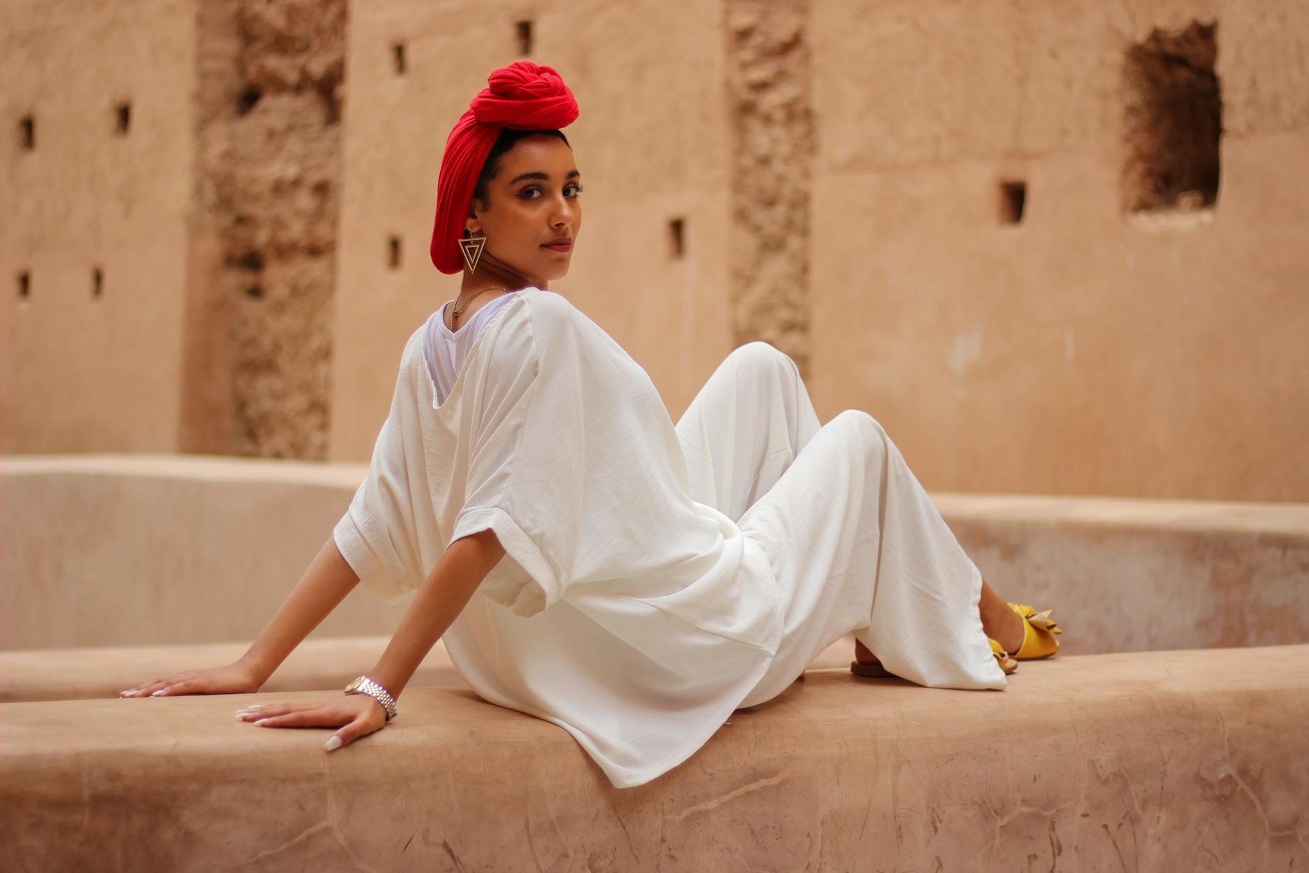 Woman in white outfit and red headscarf posing in a Marrakesh courtyard