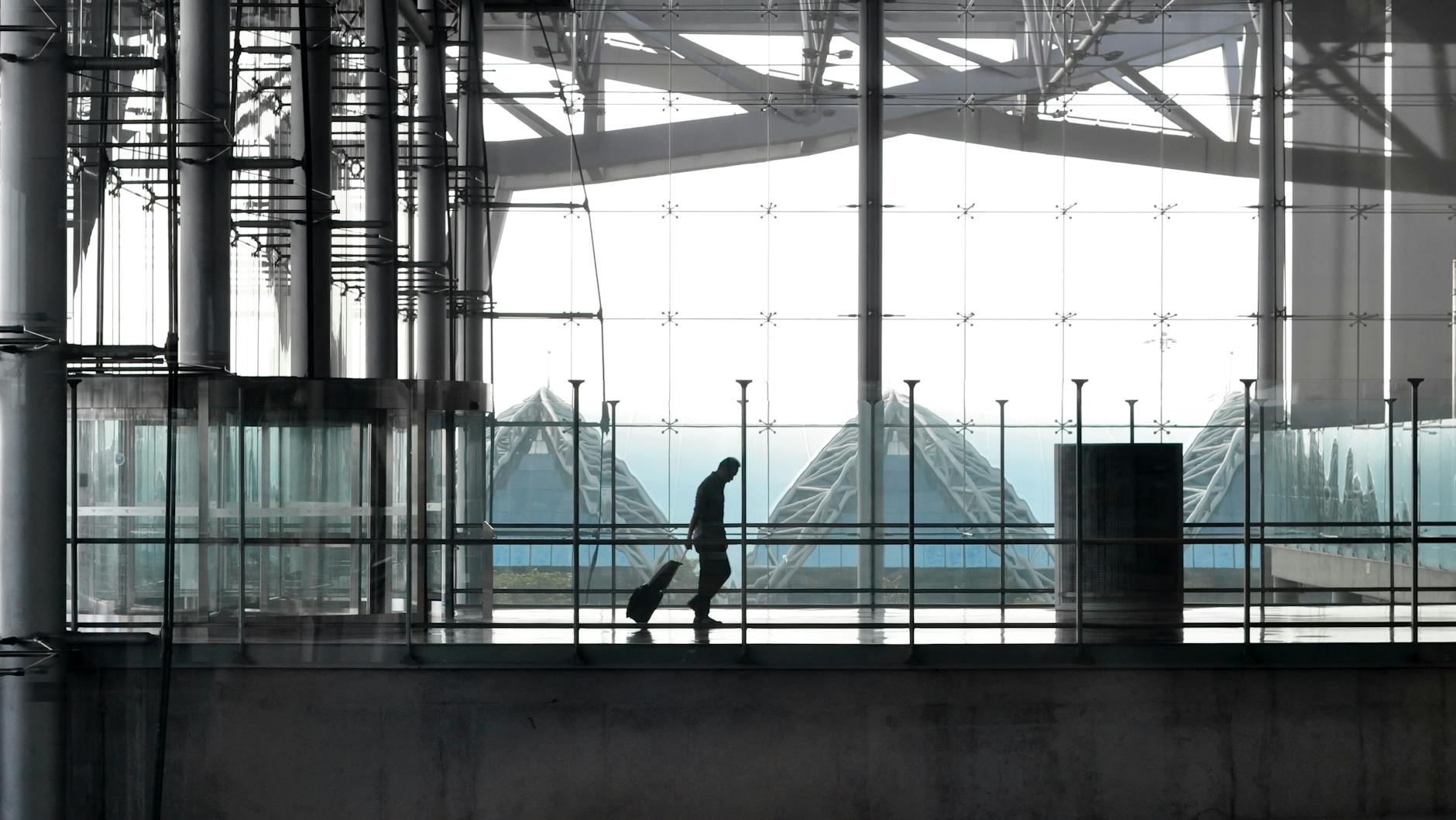 Traveler with suitcase walking through a glass airport terminal