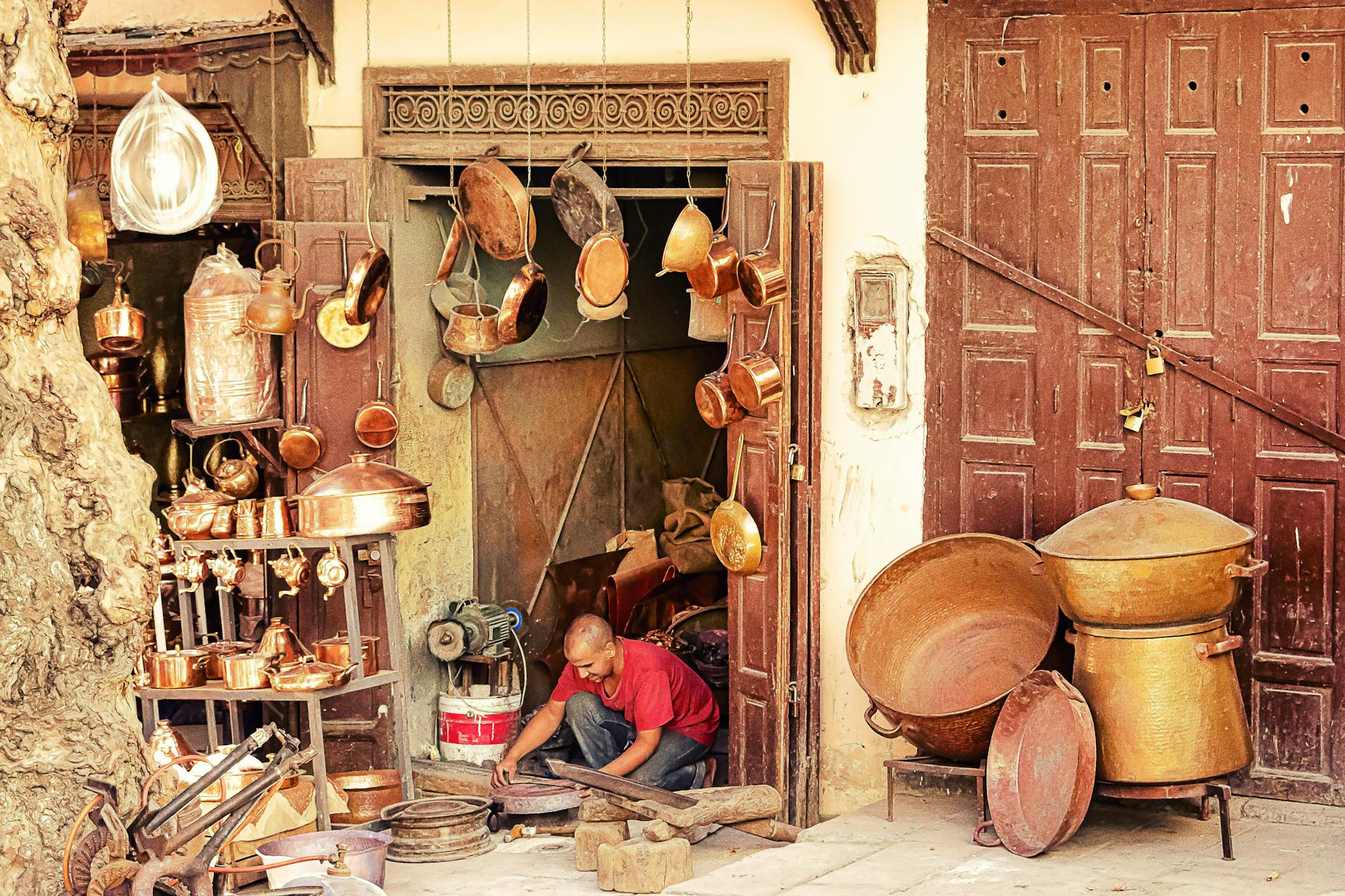 Coppersmith working outside a workshop filled with pots and pans