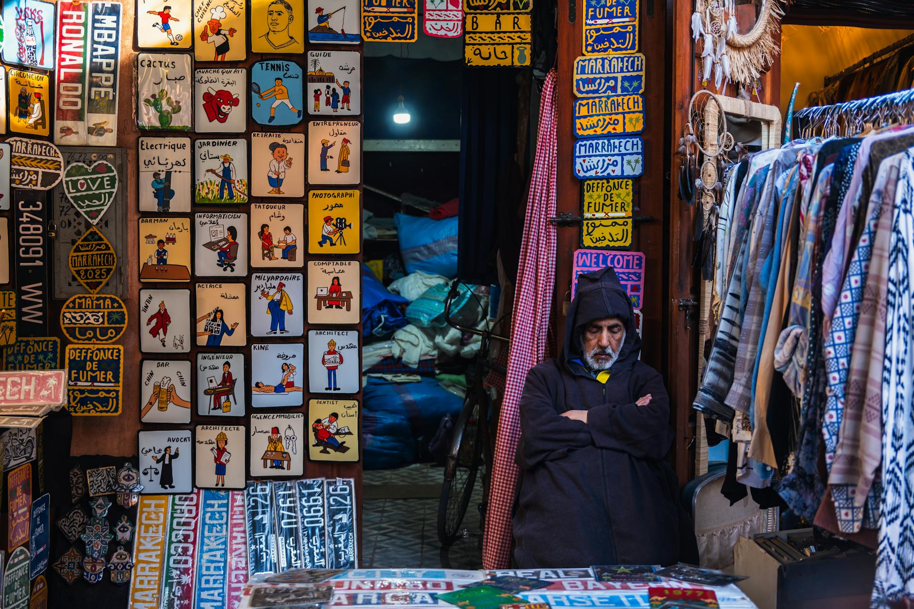 Vendor in a Marrakech souk surrounded by colorful signs and garments