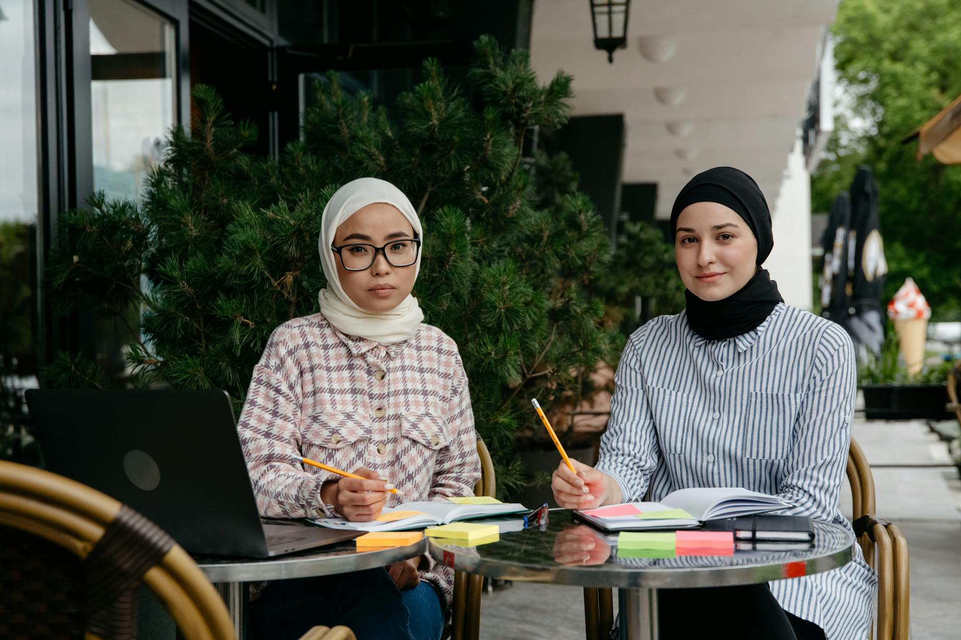 Two women studying with laptops and notebooks at an outdoor cafe