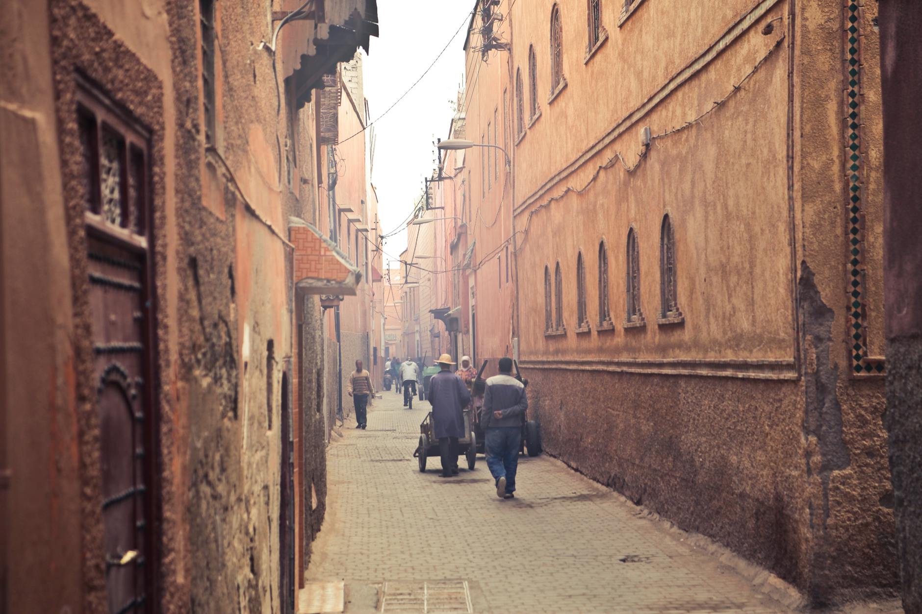 Narrow old-city street with pedestrians between weathered buildings