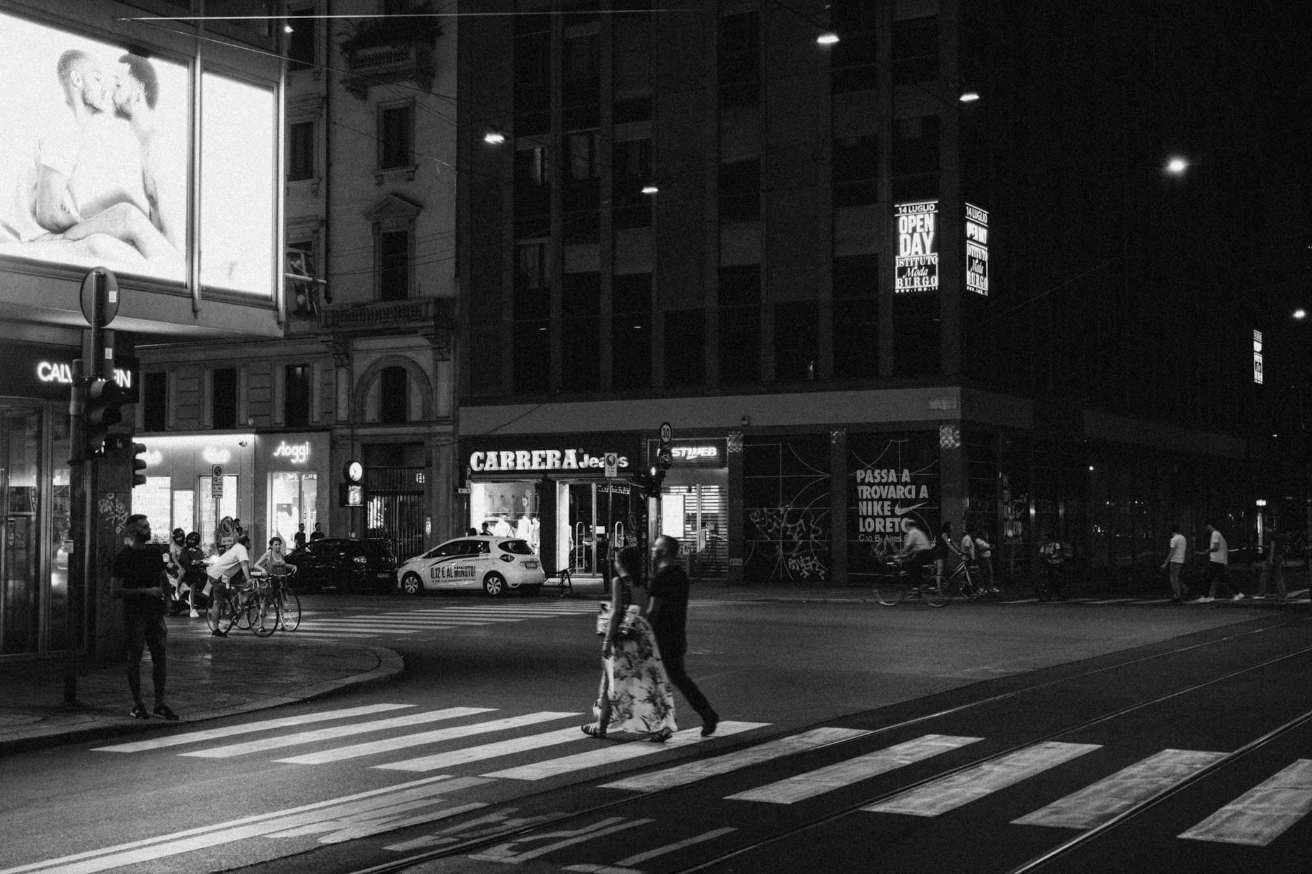 Pedestrians crossing a downtown Milan street at night