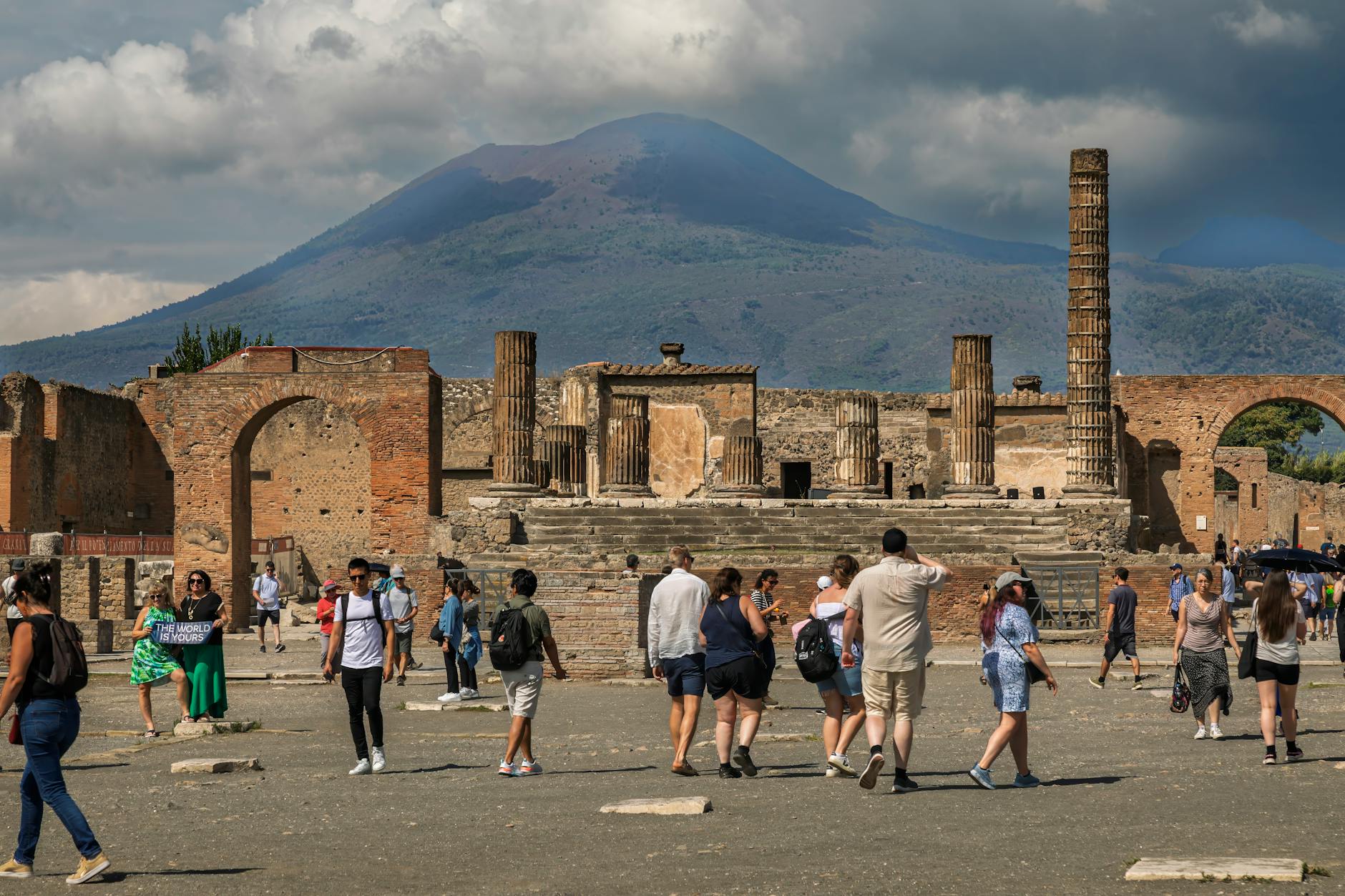 Visitors walking through Pompeii ruins with Mount Vesuvius behind