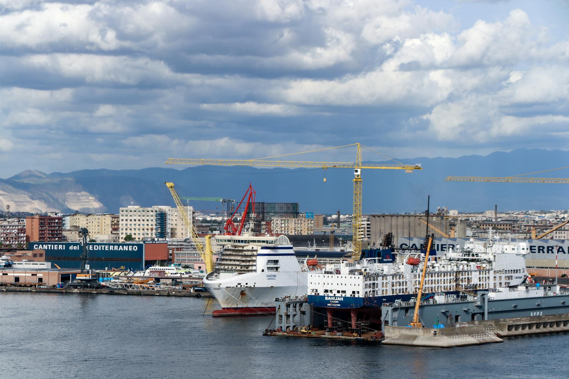 Cruise ship docked at the Port of Naples with city cranes behind it