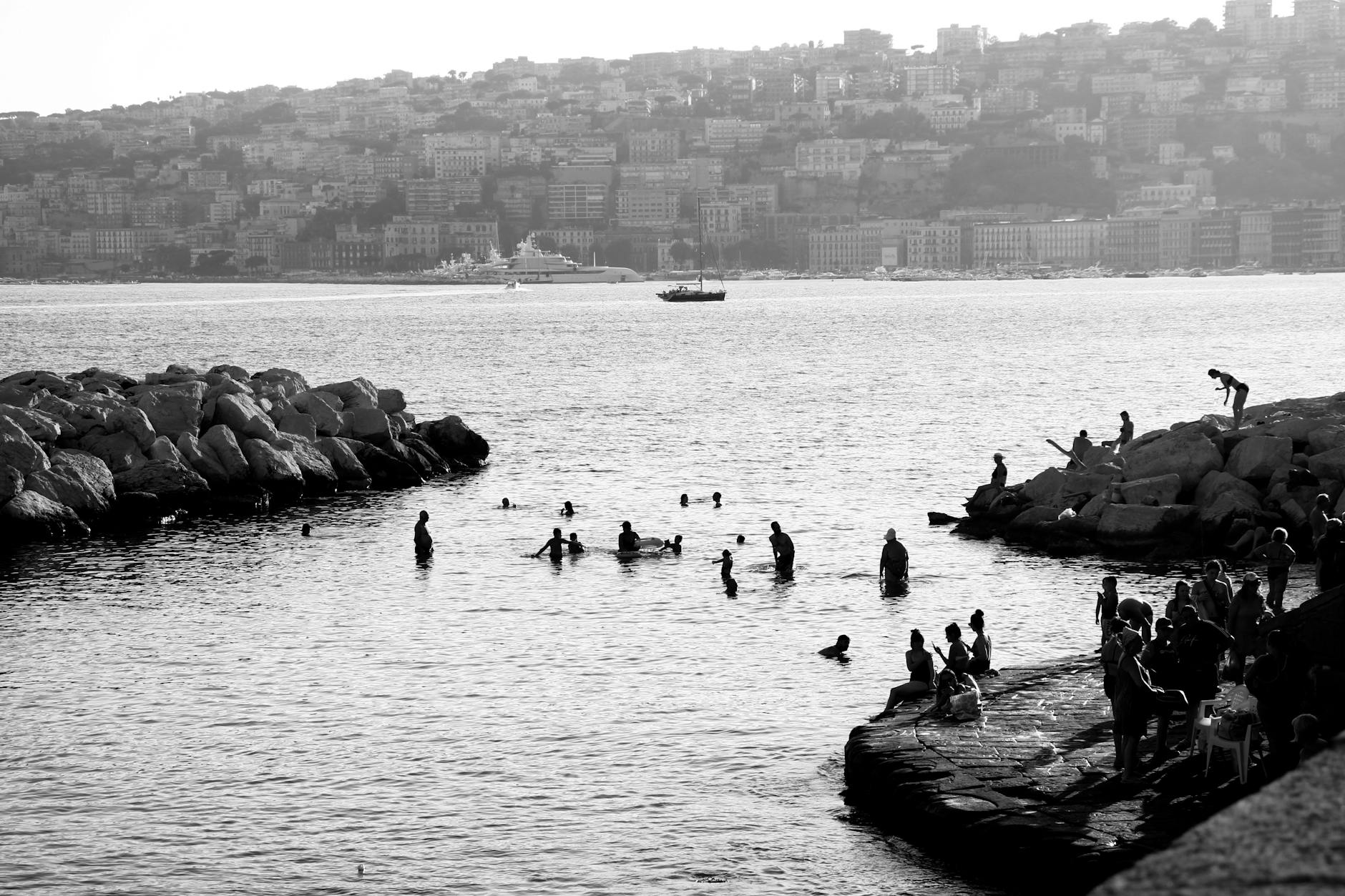 People swimming and relaxing by the rocky seaside in Naples