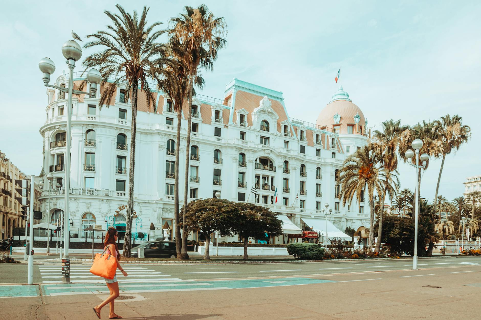 Pedestrian walking near a palm-lined hotel in Nice