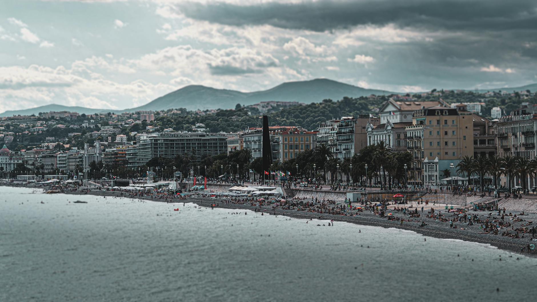 Beachfront city view with people by the sea and mountains behind Nice