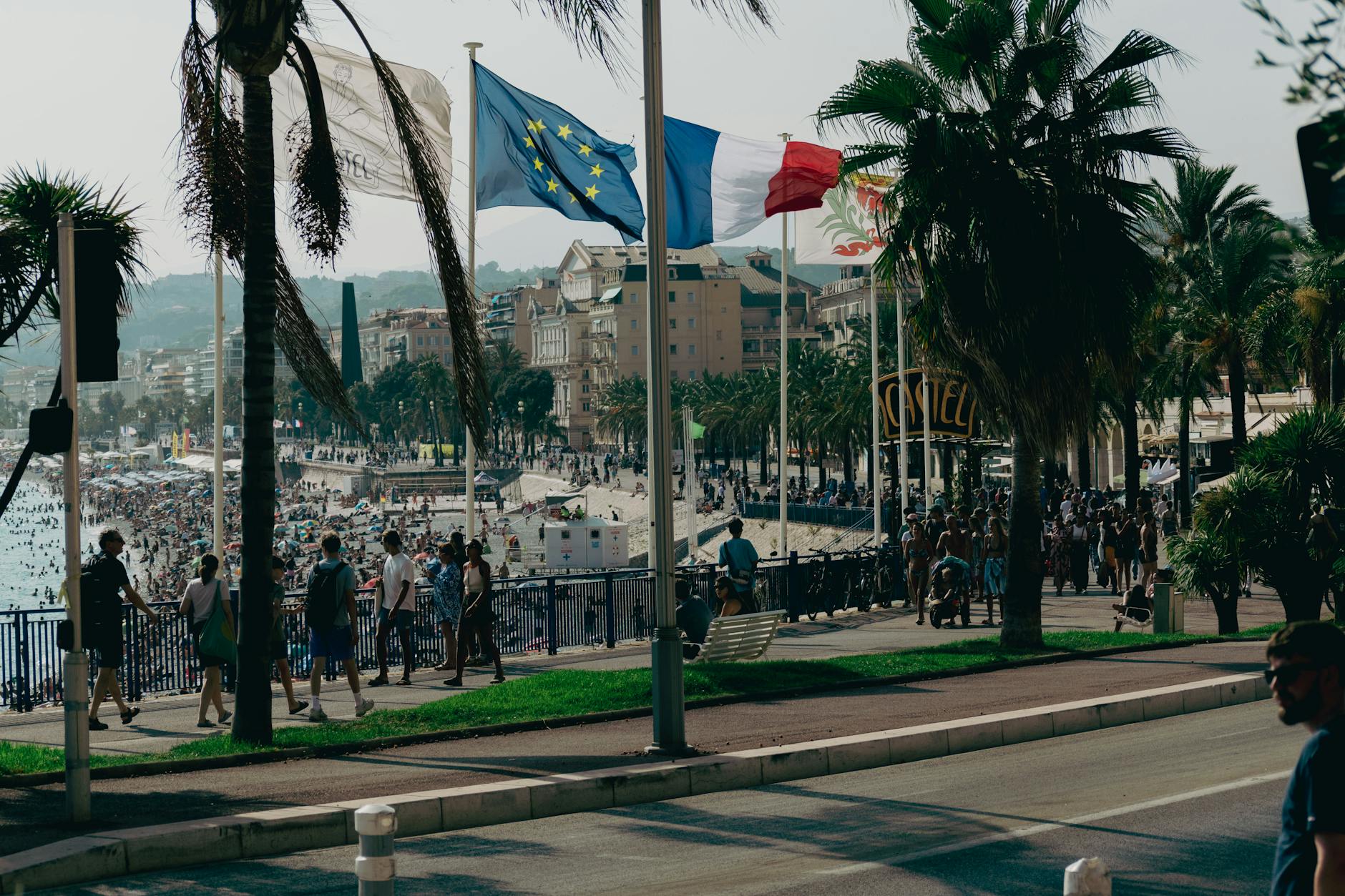 Crowded Nice waterfront promenade with flags on a summer day