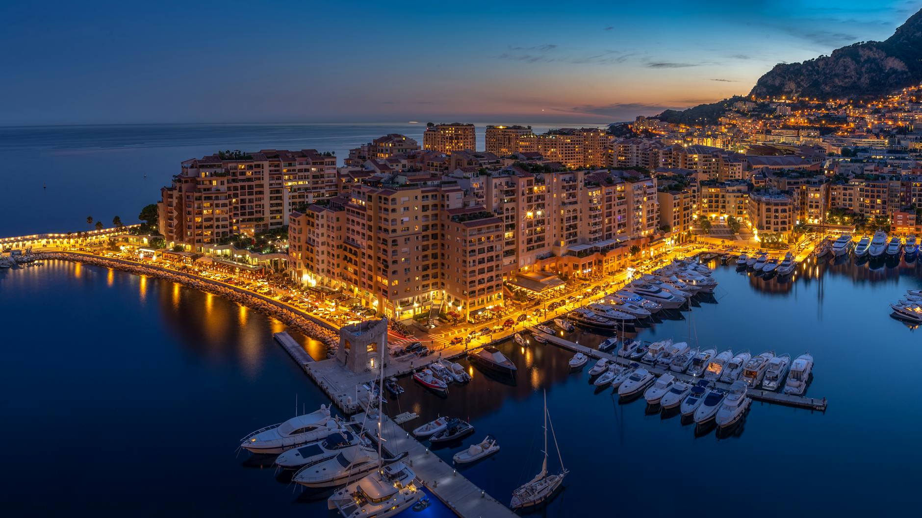 Monaco harbor at dusk with city lights and boats