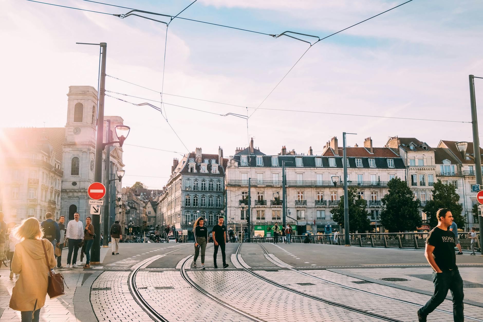 People crossing a sunny tramway intersection in a European city