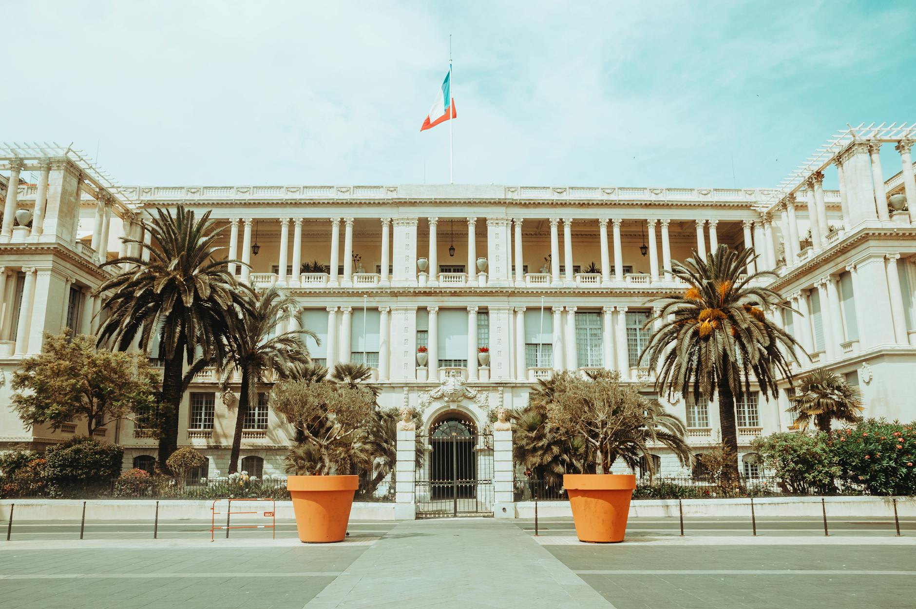 Elegant palace facade in Nice with palm trees and French flag