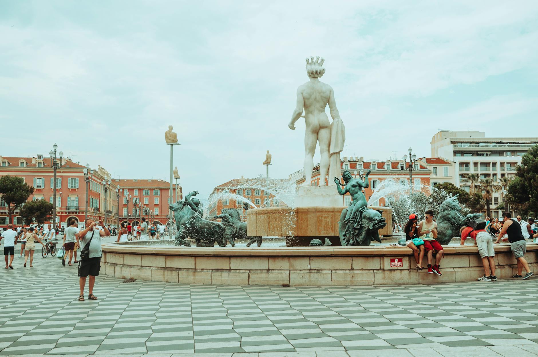 People walking through a vibrant Nice square with a fountain