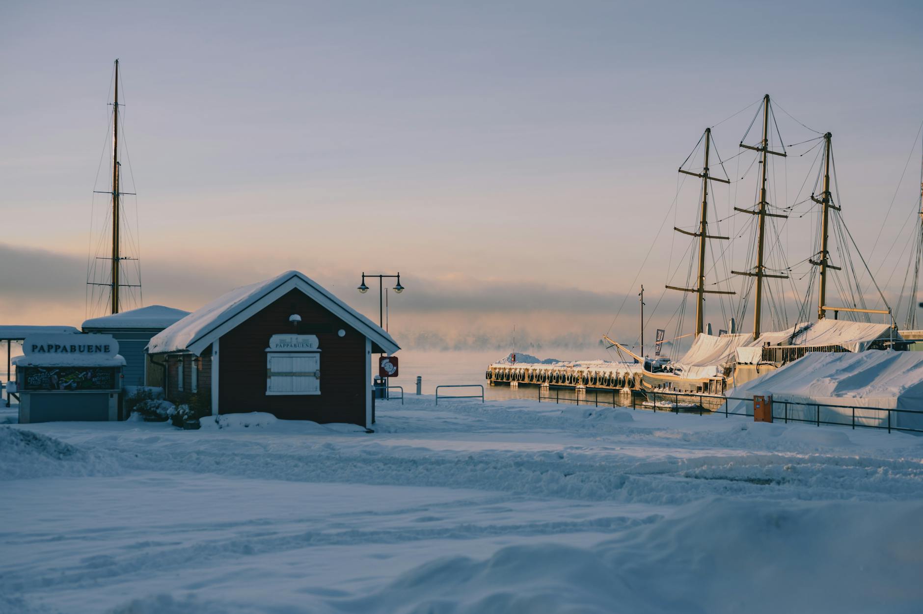 Snowy Oslo harbor with moored sailboats at sunset
