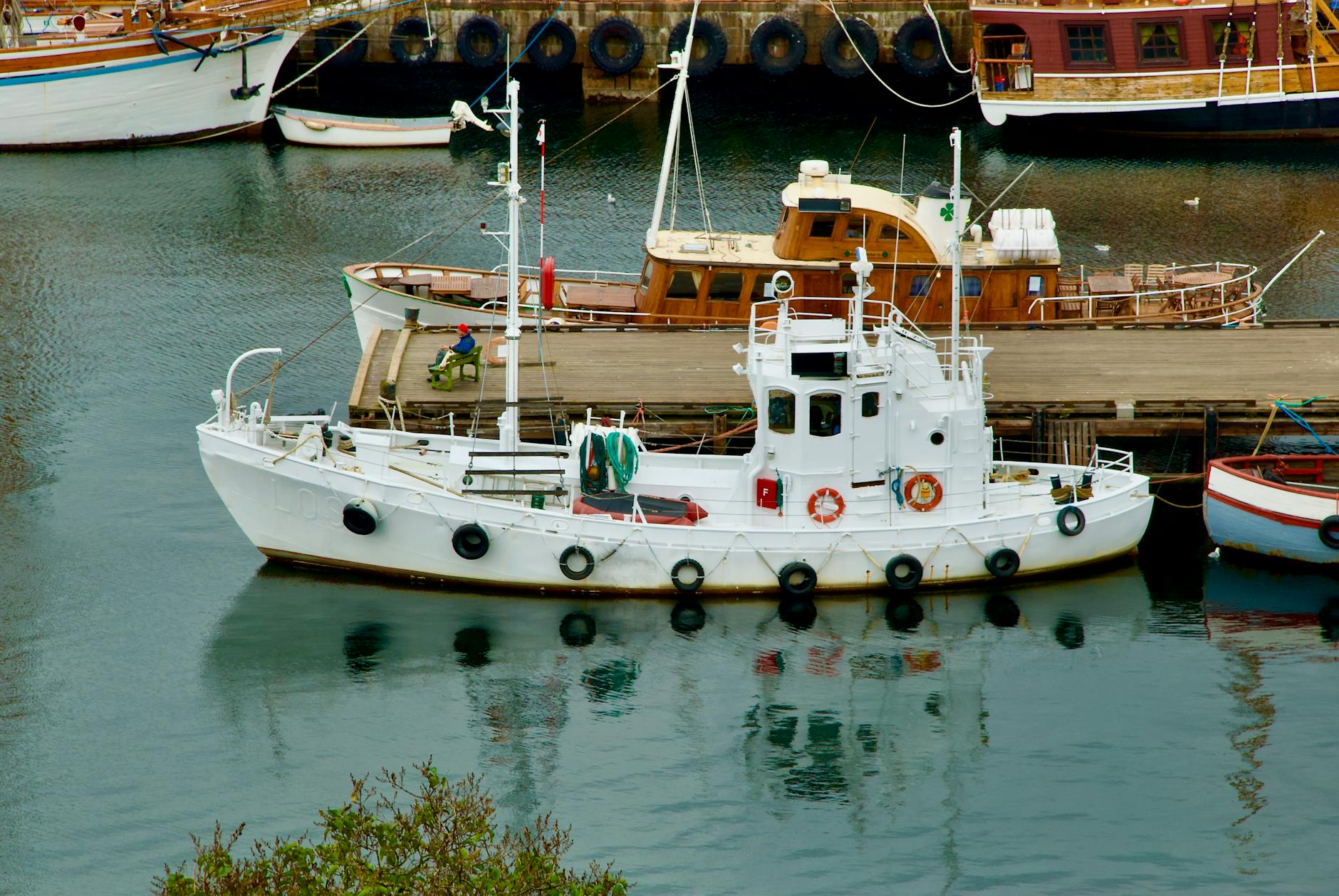 White fishing boat docked at Oslo harbor with wooden ships behind it