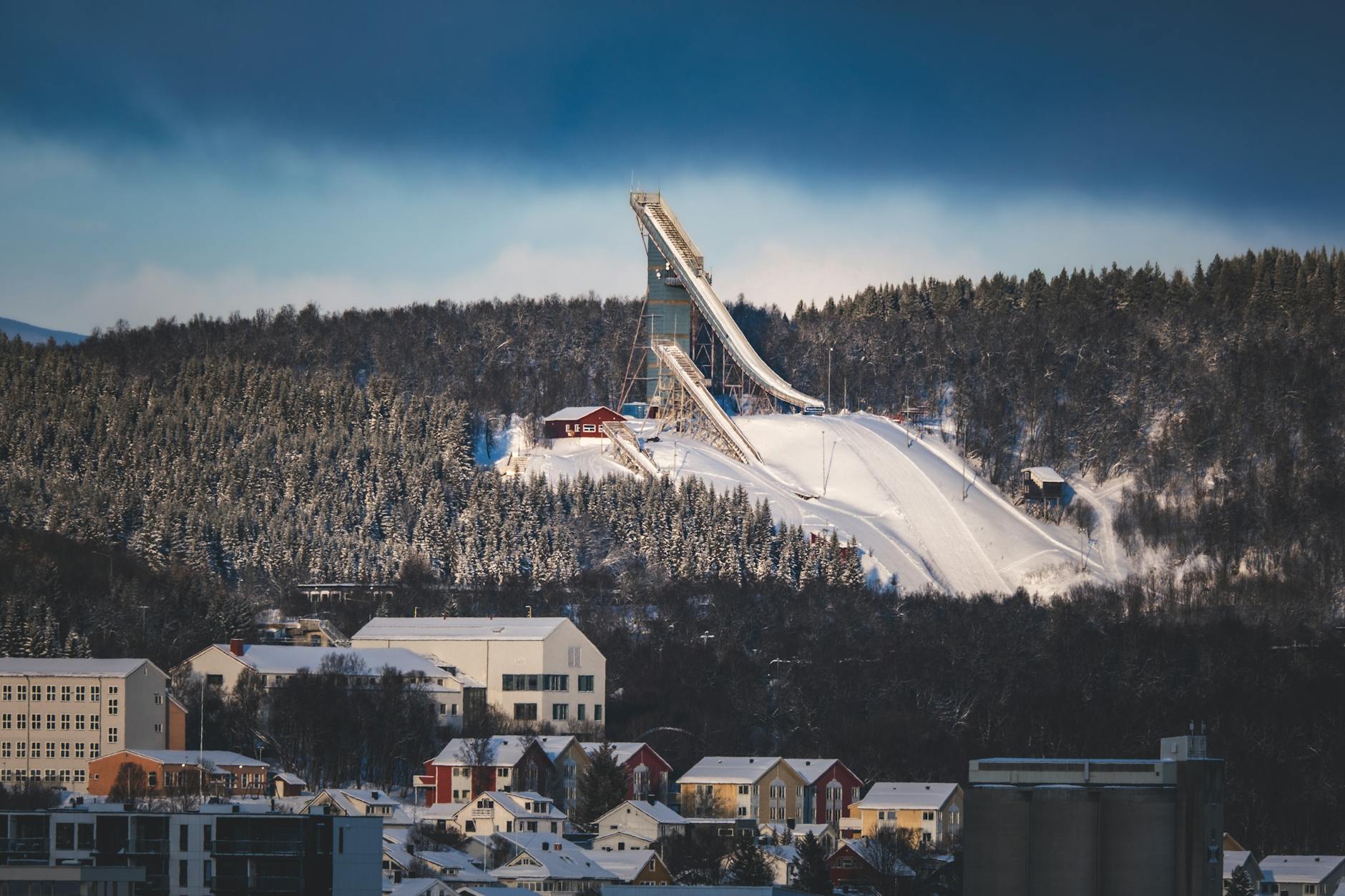Oslo ski jump surrounded by snowy forest and city buildings