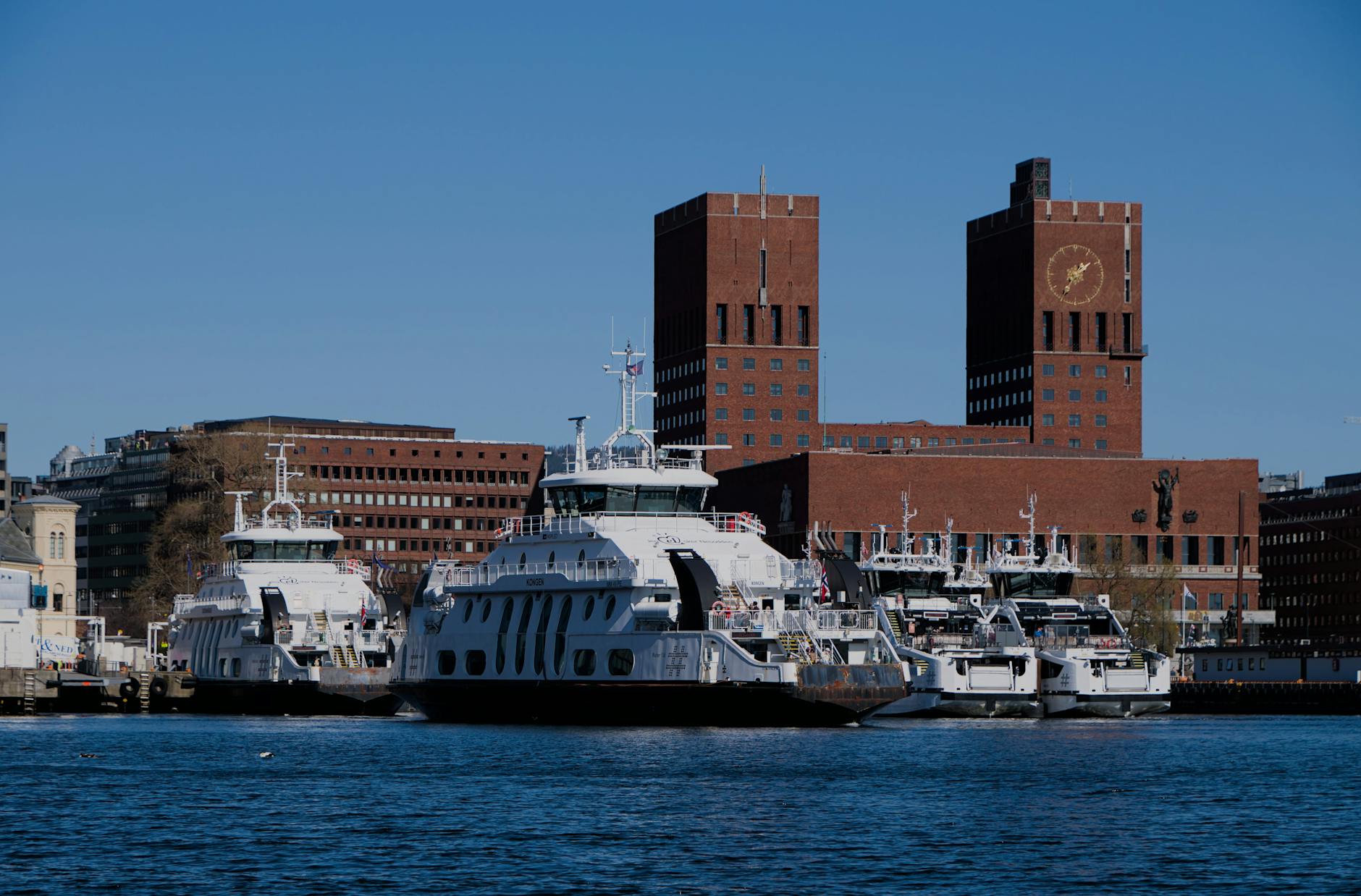 Ferries docked by Oslo City Hall under a clear sky