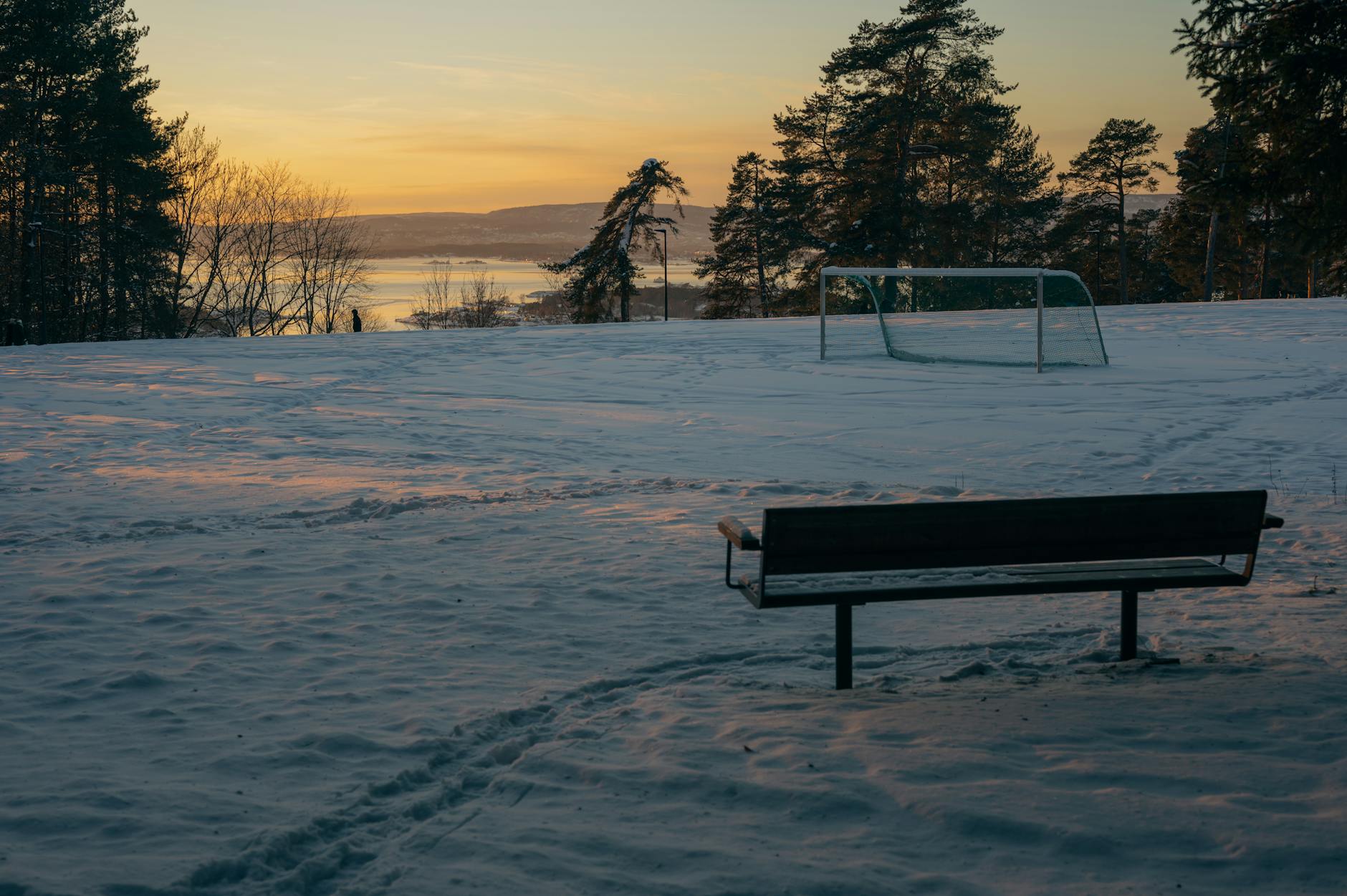Snowy Oslo park bench at winter sunset