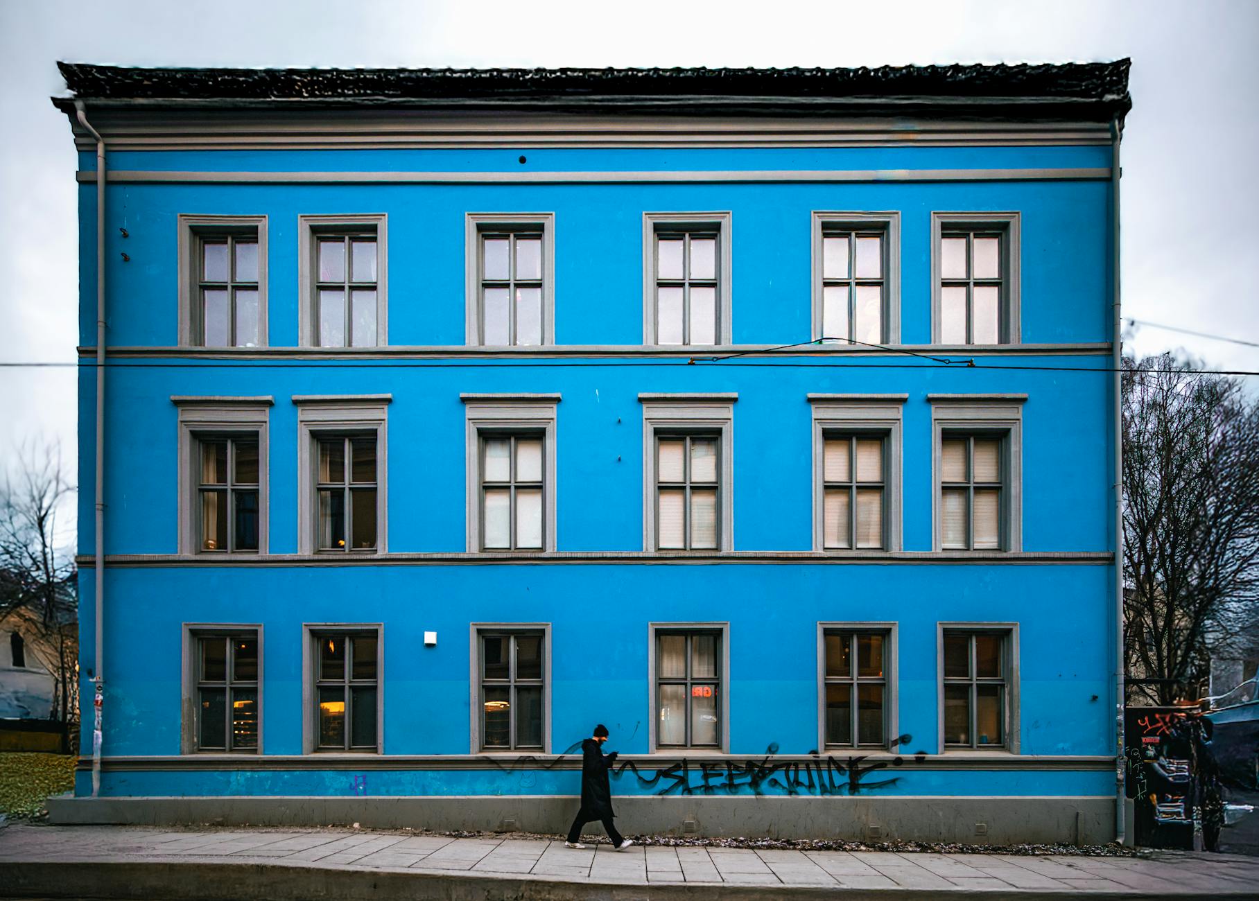Person walking past a blue urban building in Oslo