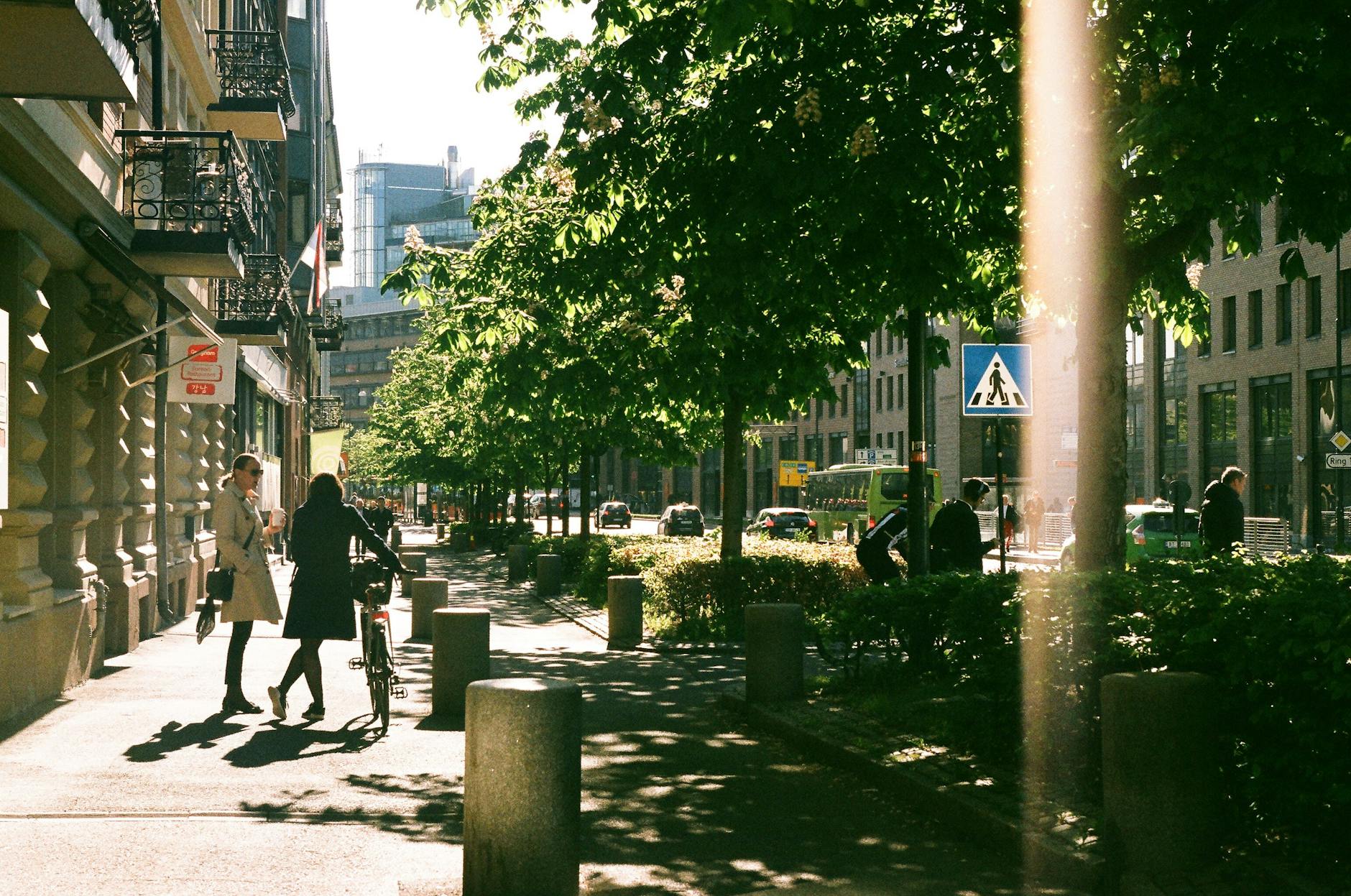 People walking on a sunlit Oslo sidewalk